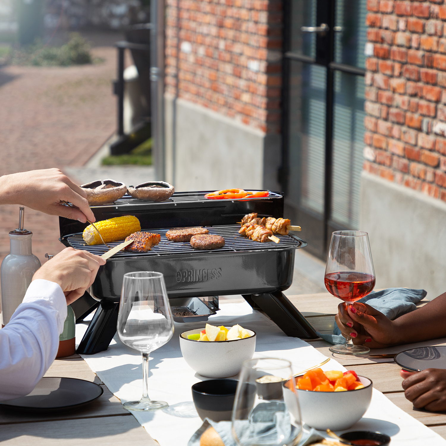Persone che grigliano cibo su una piccola griglia nera all'aperto. Include verdure e carne.