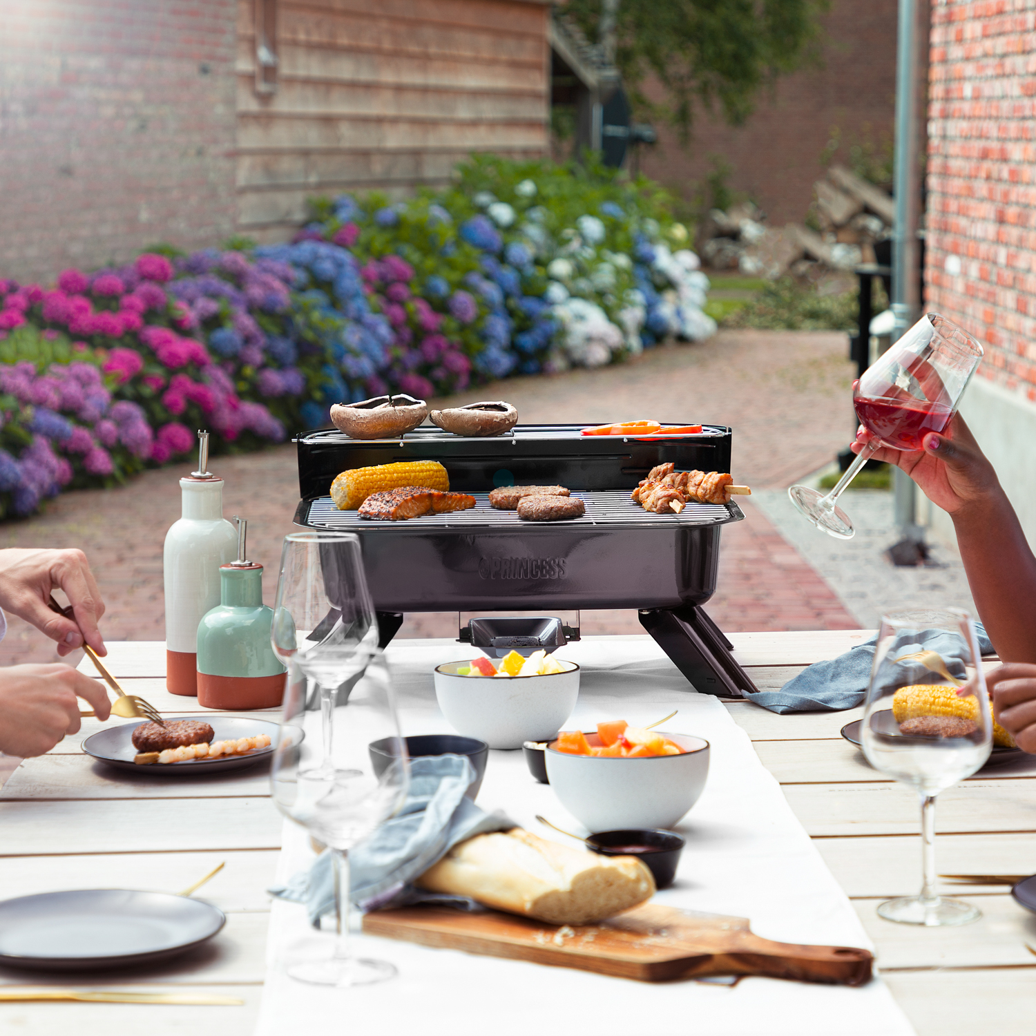 Scena barbecue all'aperto. Cibo in cottura, persone e un giardino sullo sfondo.