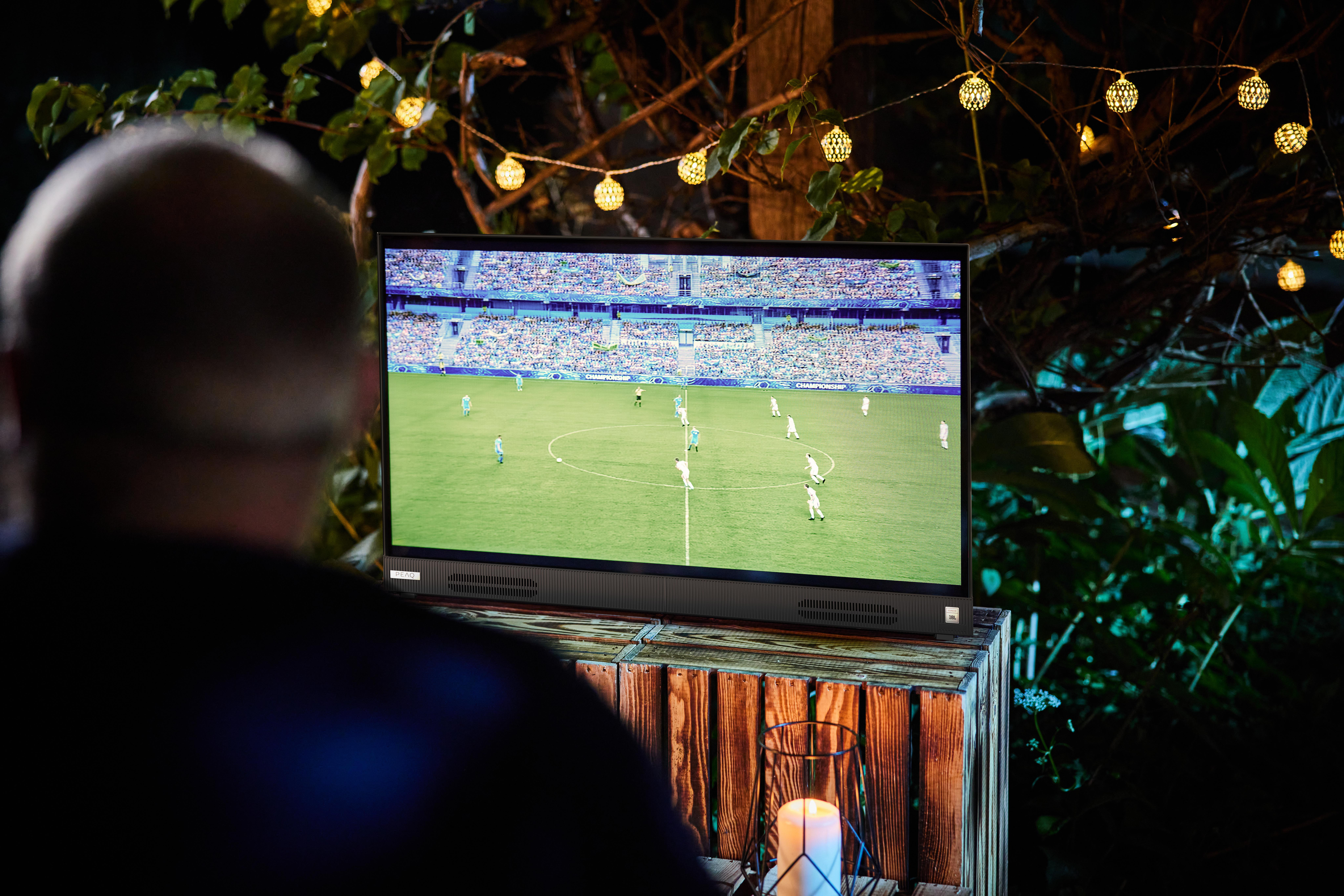 Mann, der im Freien bei Nacht ein Fußballspiel im Fernsehen ansieht.