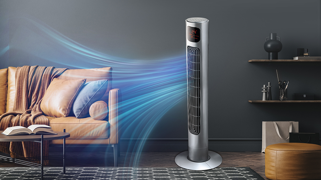 Magas ezüst ventilátor digitális kijelzővel, levegőt fúj a kanapé és a könyvek felé.