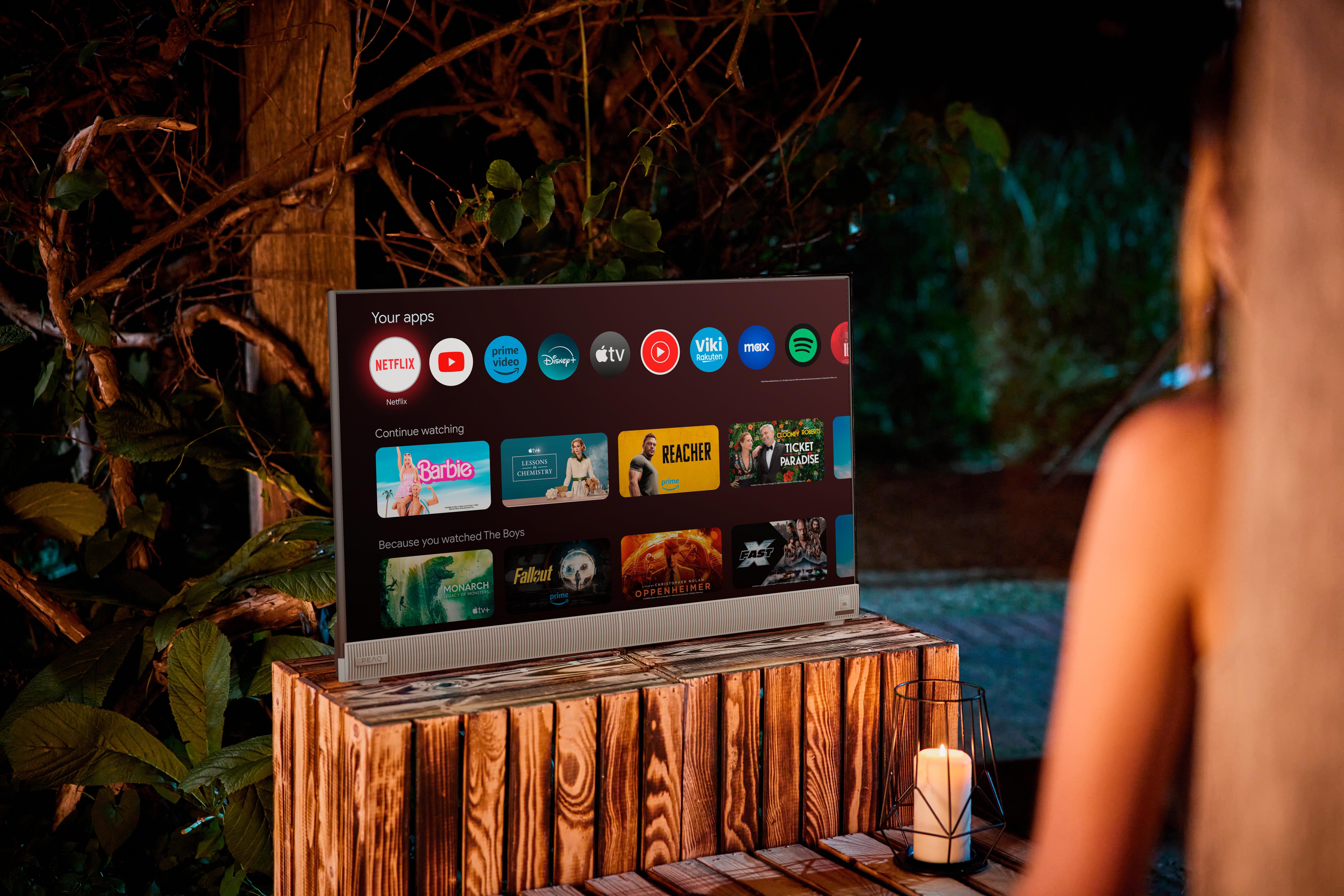 Ein Fernsehbildschirm, der Apps auf einem Holzständer zeigt, mit einer Person im Hintergrund.
