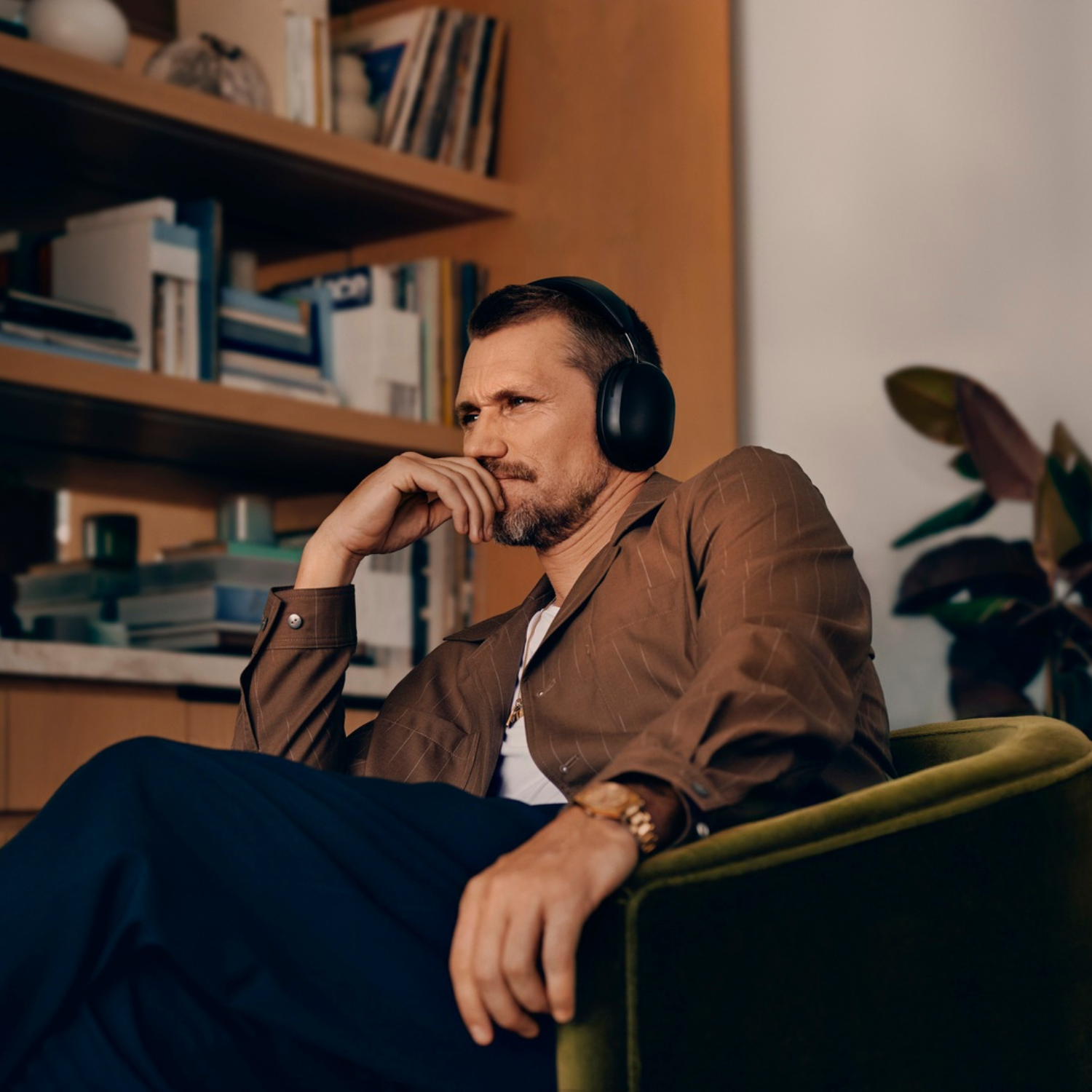 Hombre con auriculares, sentado en una silla verde, con aspecto pensativo.