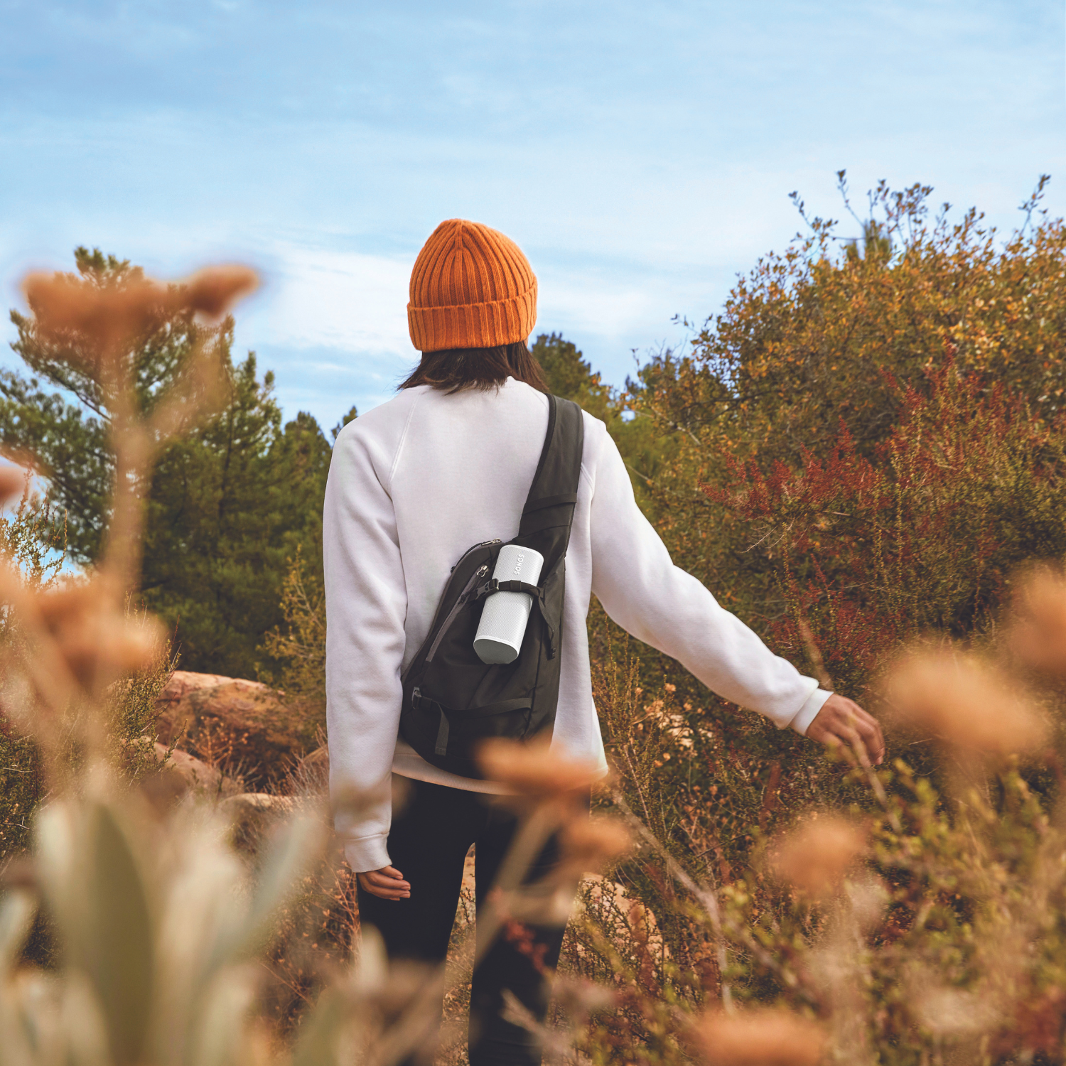 Mujer caminando en la naturaleza, llevando un recipiente blanco en una bolsa negra.