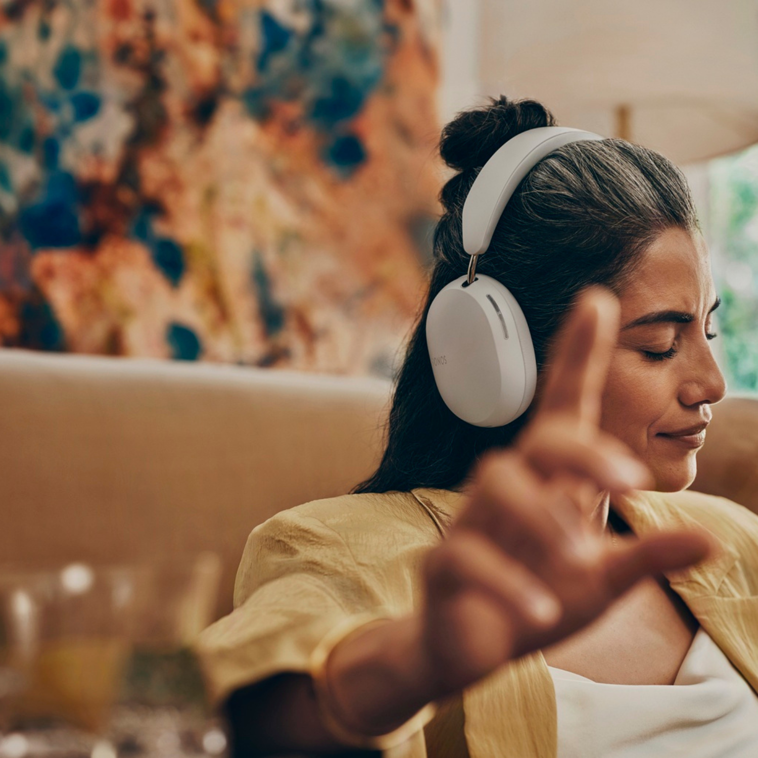 Mujer con auriculares blancos, gesticulando con la mano. Relajada en interiores.