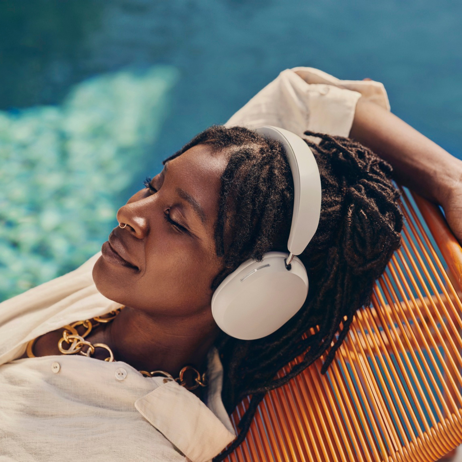Mujer con auriculares, relajándose junto a una piscina.
