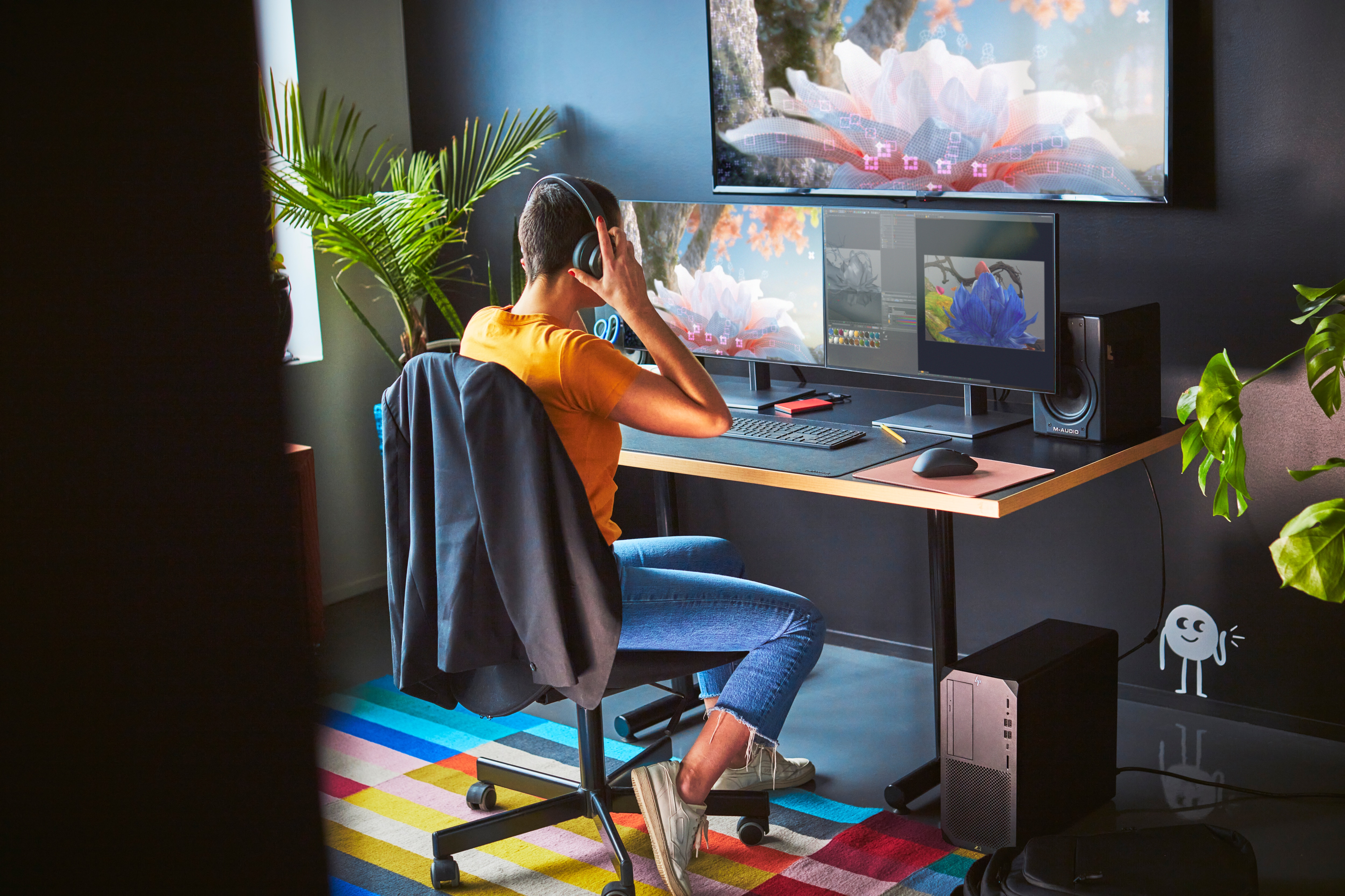 Una persona con auriculares trabaja en un escritorio con dos monitores y una computadora.