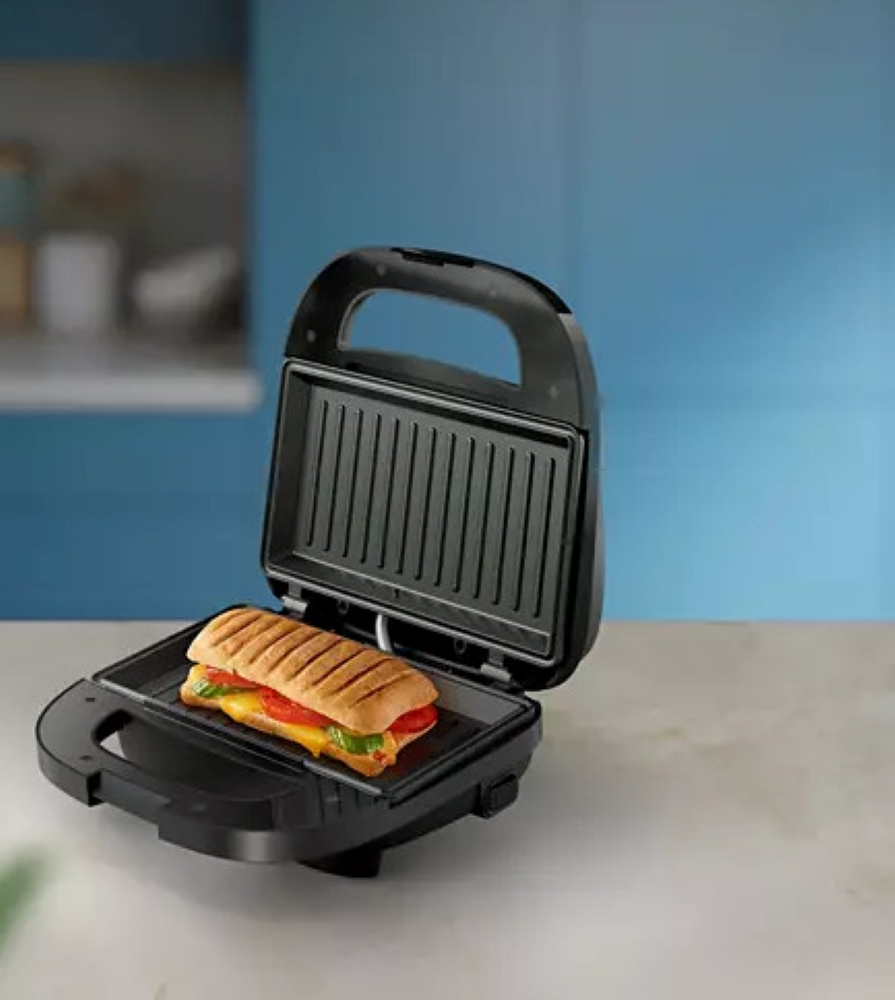 Toster do kanapek z gotową kanapką w środku. Urządzenie czarne, kanapka złocista.
