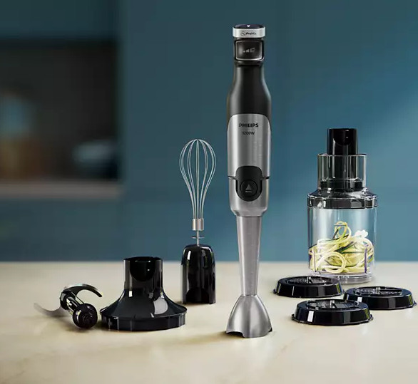 Srebrny i czarny blender ręczny z przystawkami na stole, na rozmytym tle.