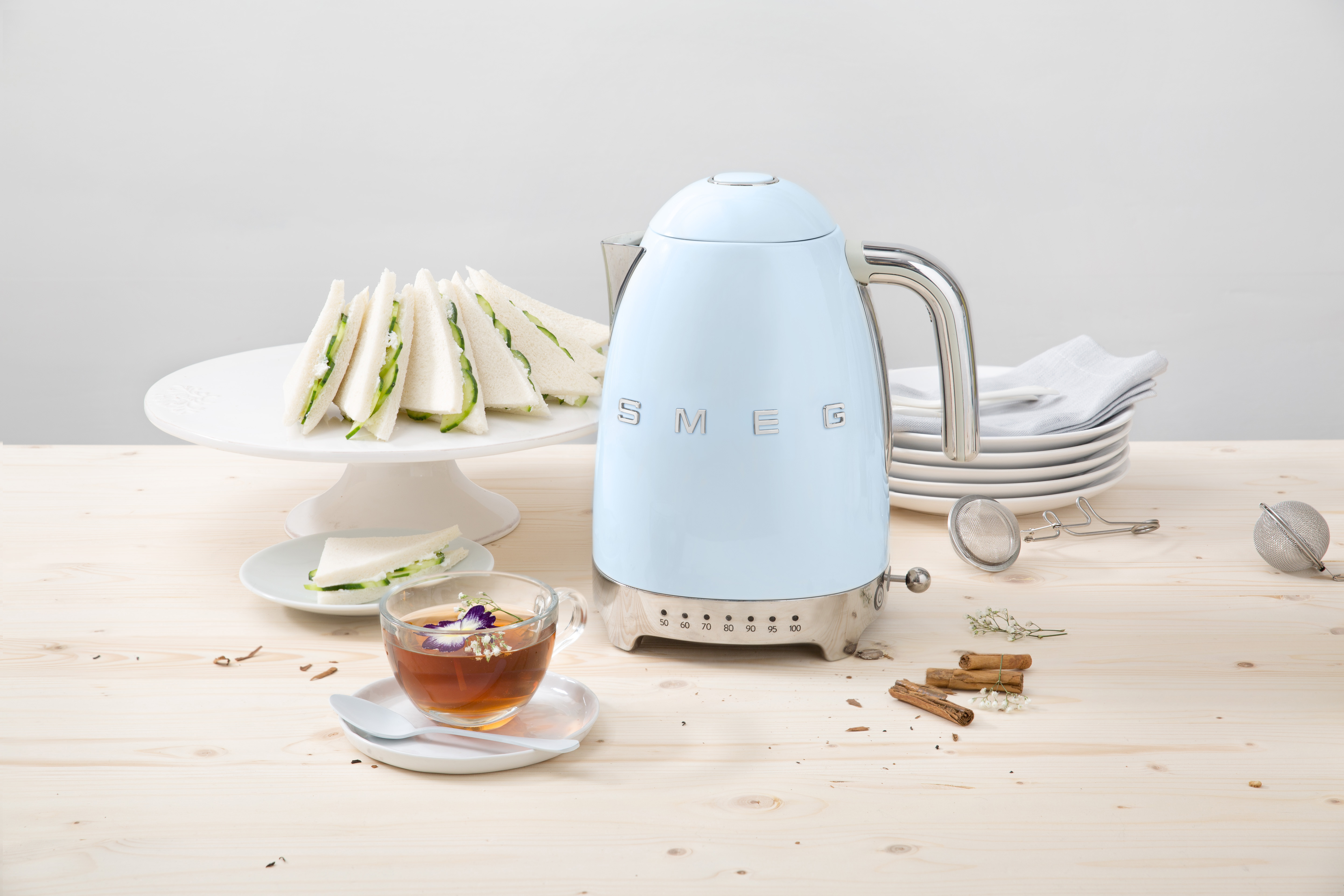 Hellblaue Kanne mit Tee, Sandwiches und anderen Gegenständen auf einem Holztisch.