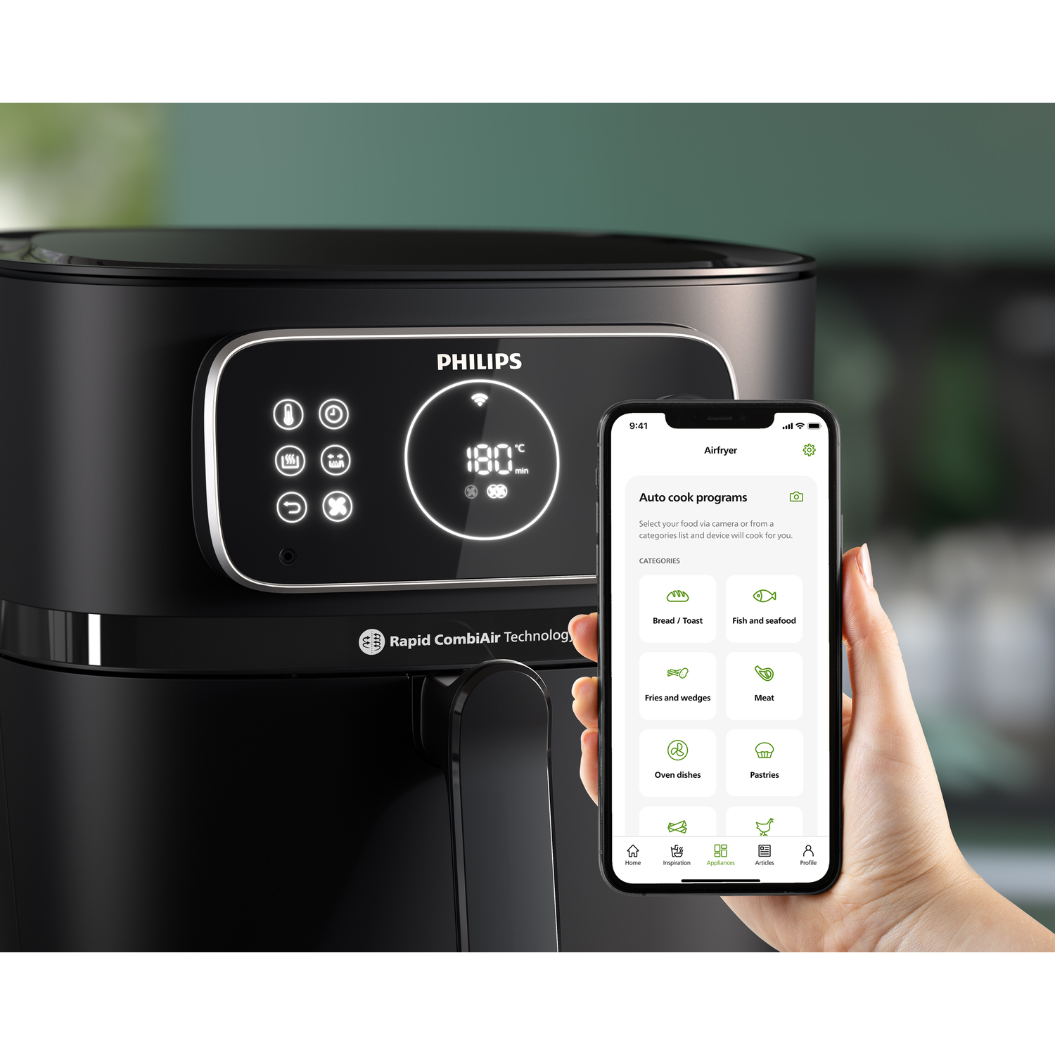 A black Philips Airfryer with a person holding a phone showing recipes.