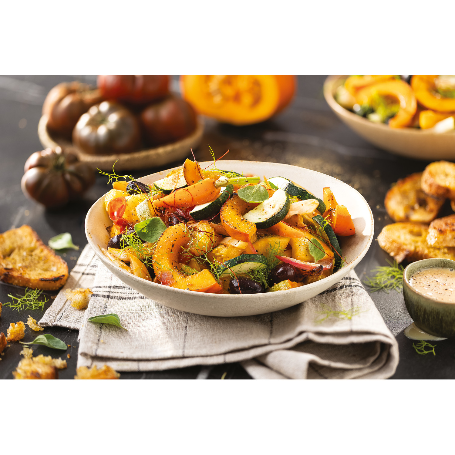 Bowl of roasted vegetables with croutons and sauce on a table setting.
