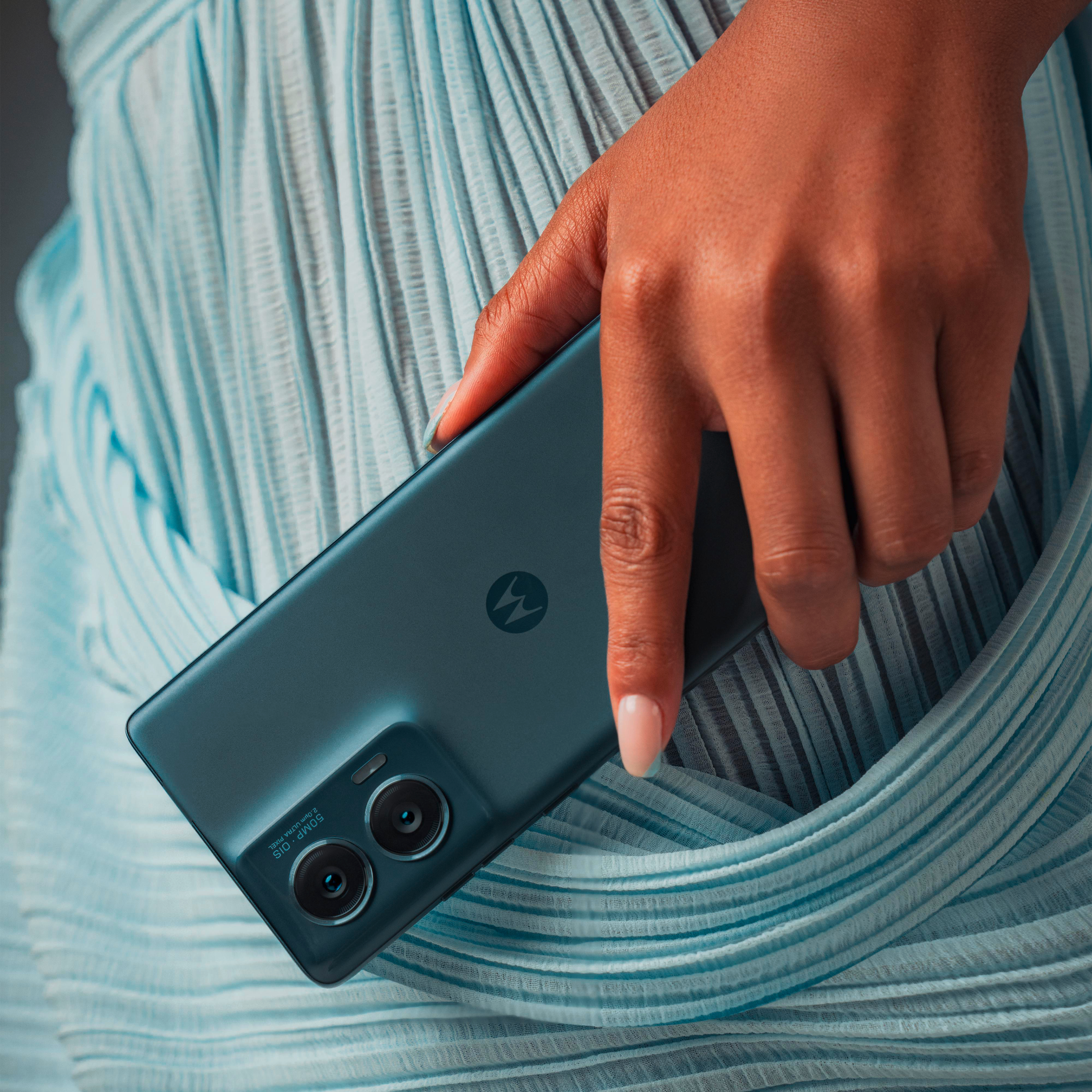 Une main tient un téléphone bleu foncé, avec une caméra à double lentille.