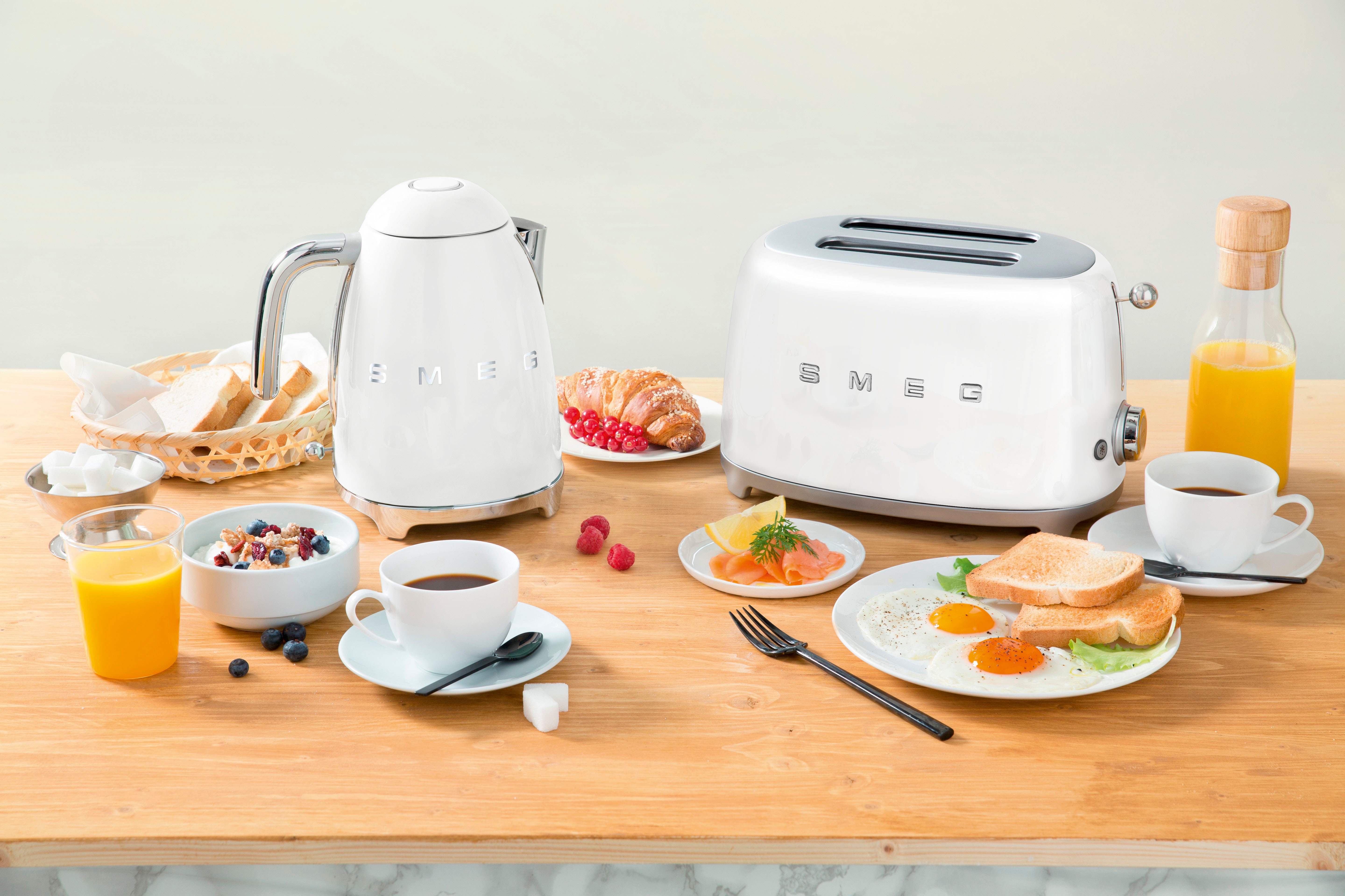 Un petit-déjeuner avec des appareils blancs, des aliments et du jus sur une table en bois.