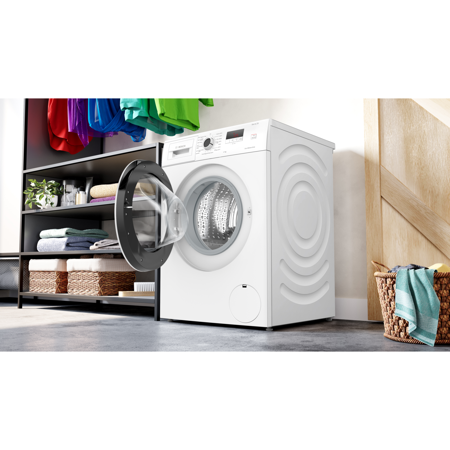 White washing machine with open door, inside a room with shelves and a basket with towels.