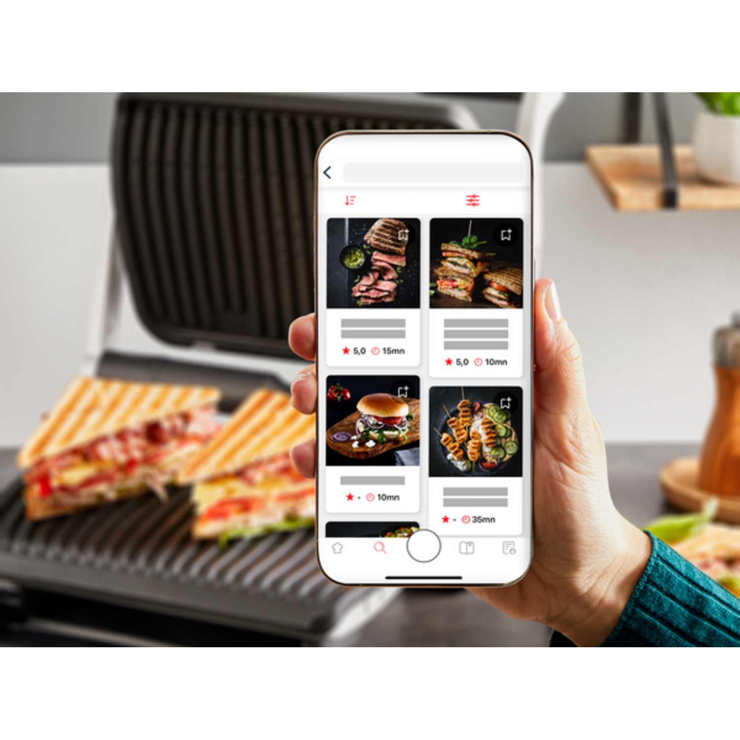 A hand holding a phone displaying recipes with a grill in the background.
