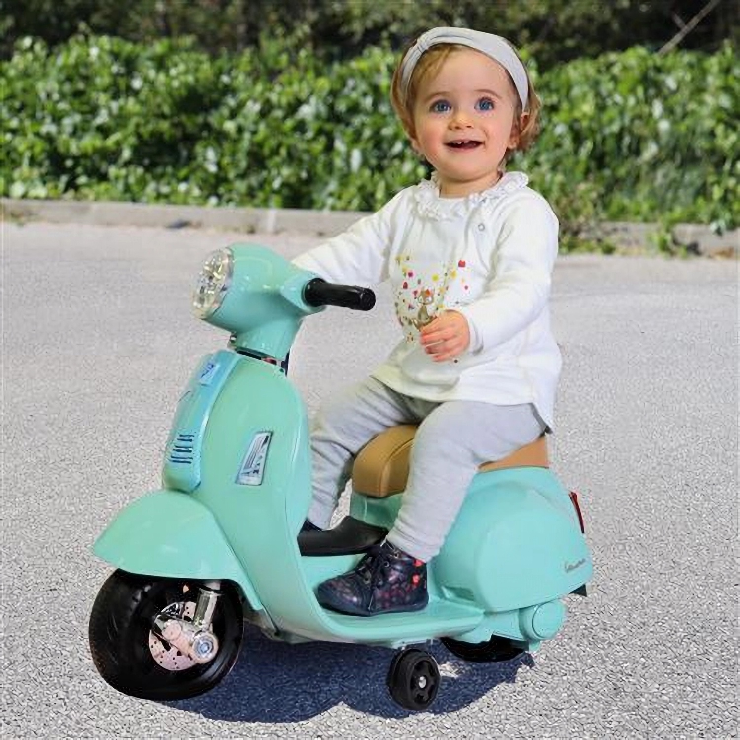 A baby on a light blue toy scooter. The baby is smiling and looking at the camera.