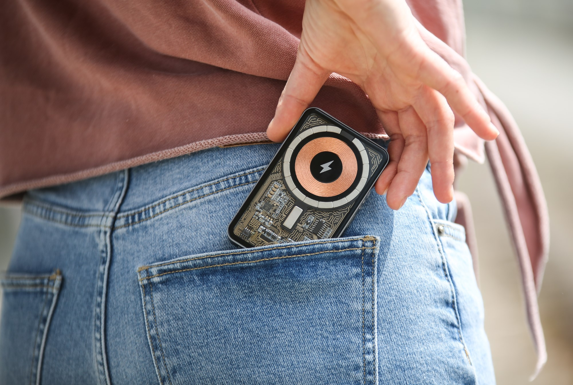 Ręka wkładająca czarne i miedziane urządzenie do kieszeni dżinsów. Urządzenie posiada cewkę ładującą.