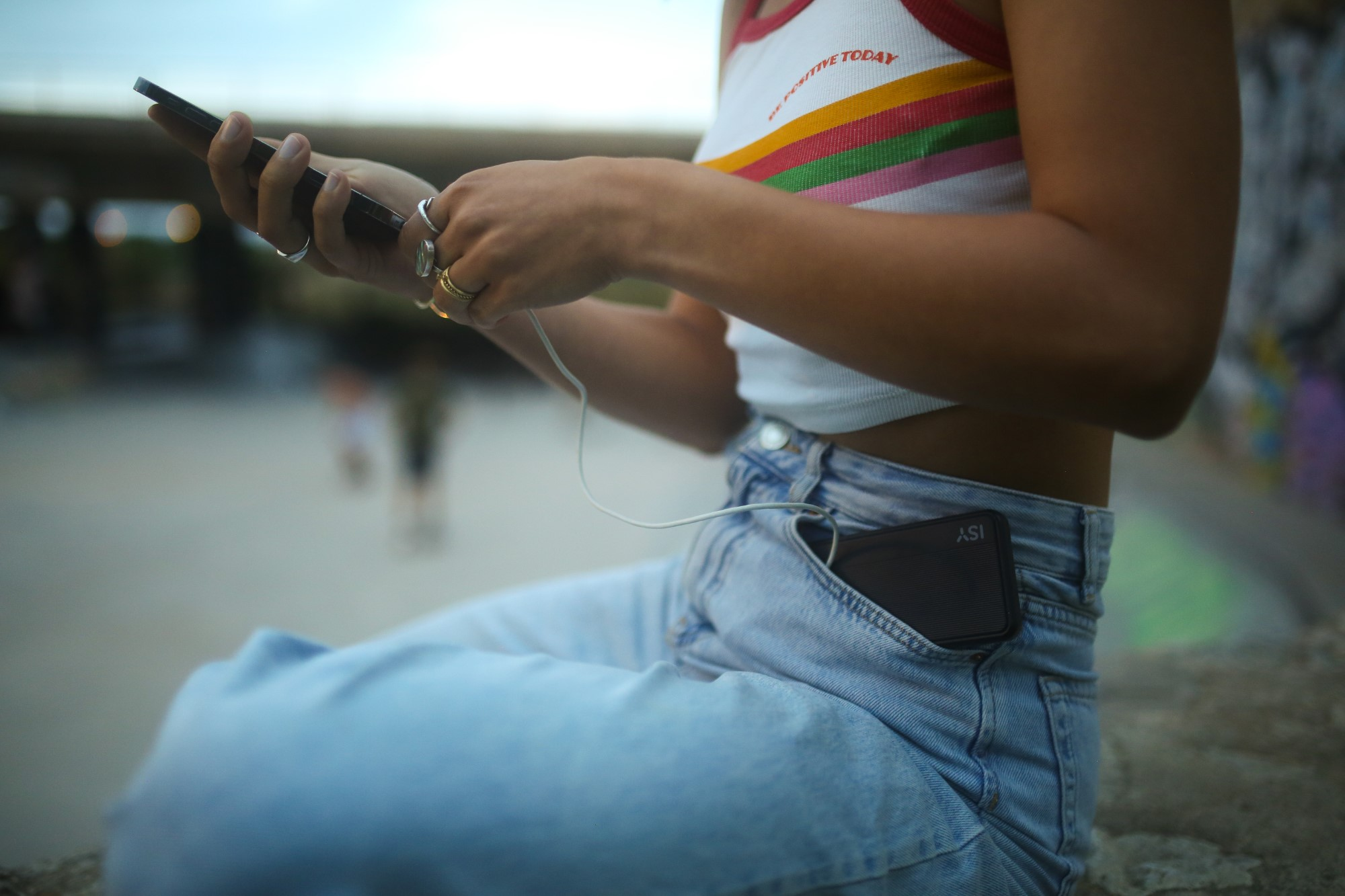 Osoba w dżinsach trzymająca telefon z ładowarką. Telefon w kieszeni.