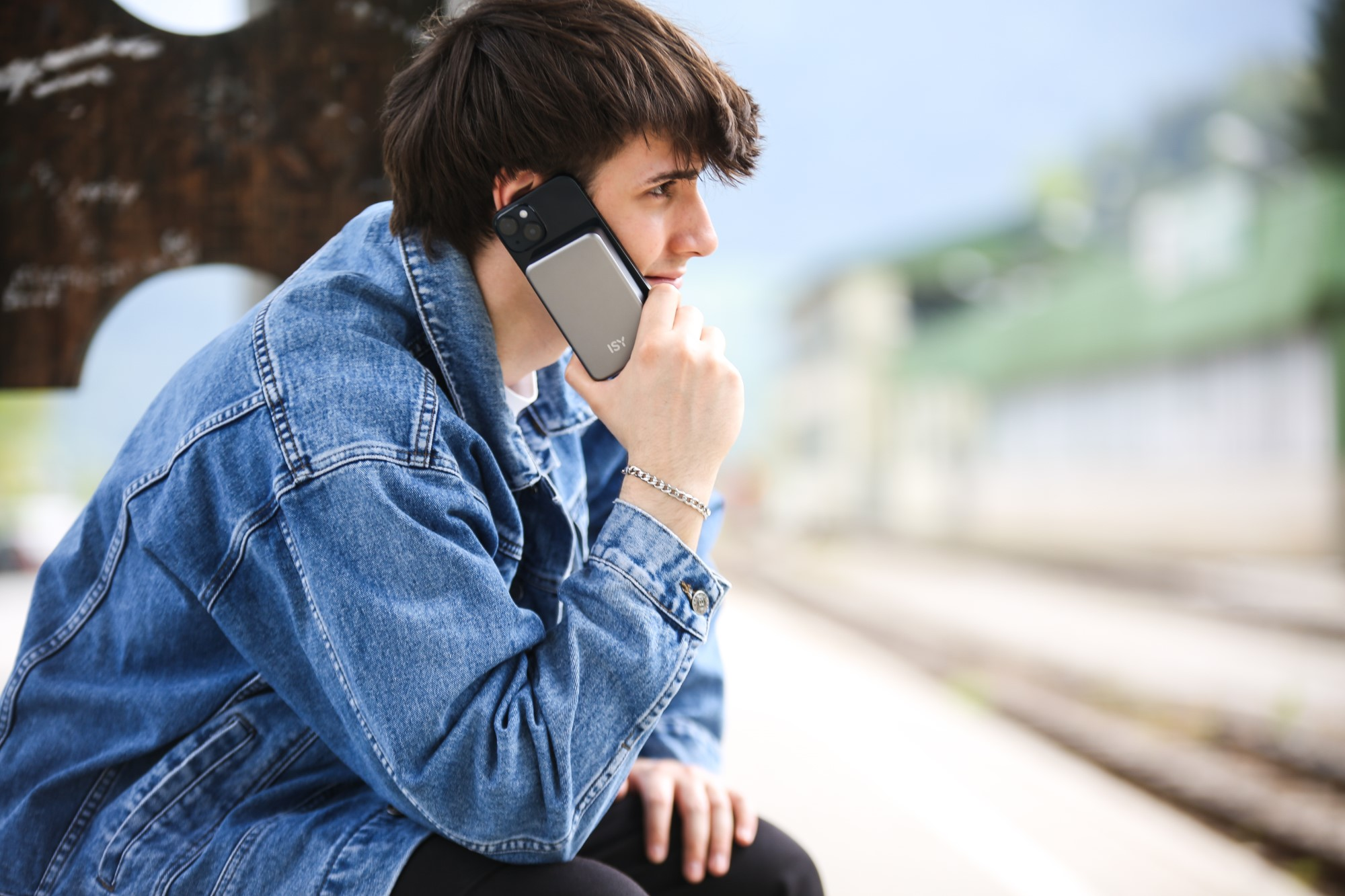 Mężczyzna w dżinsowej kurtce rozmawia przez telefon na zewnątrz.