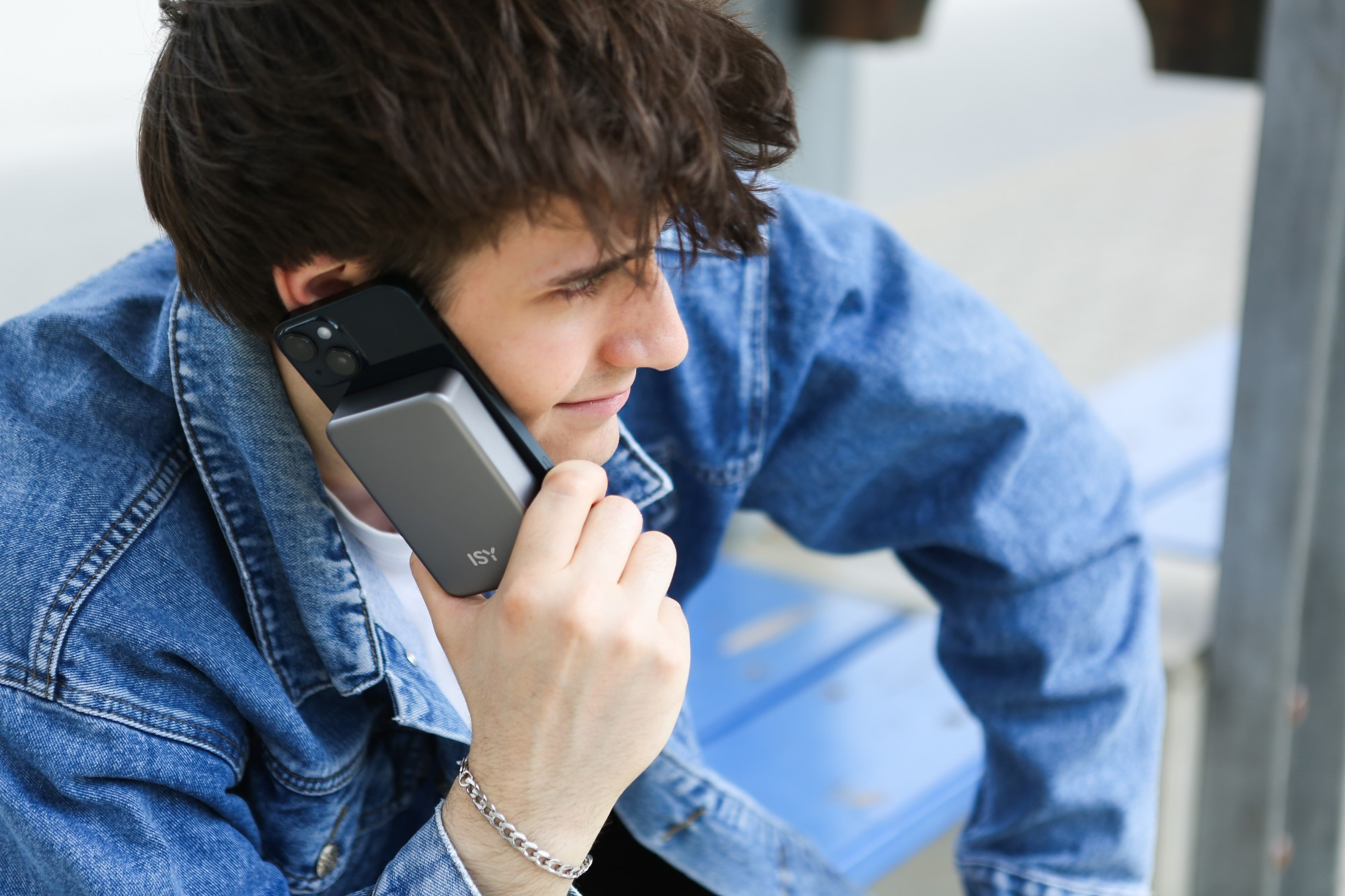 Mężczyzna trzymający telefon przy uchu, w dżinsowej kurtce. Do telefonu podłączony jest power bank.