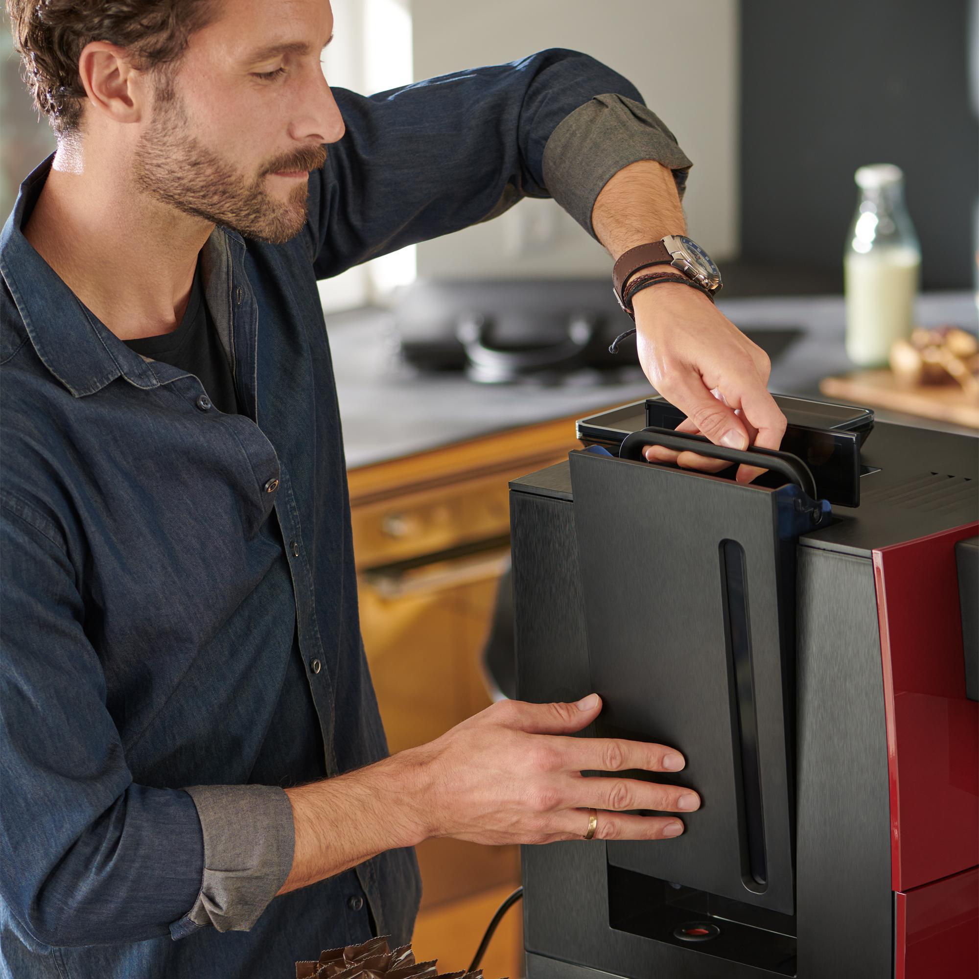 Ein Mann befüllt den Wassertank einer rot-schwarzen Kaffeemaschine.