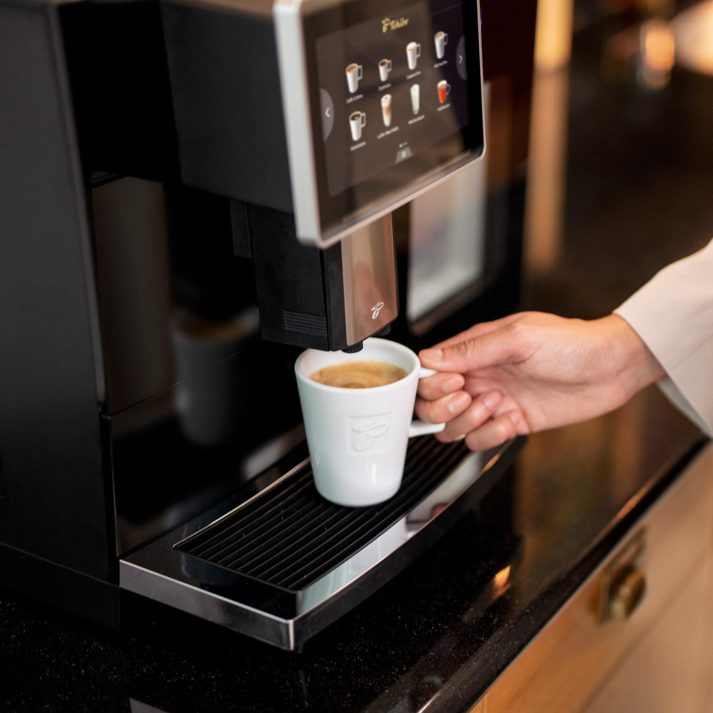 Eine Person, die Kaffee mit einer schwarzen Tchibo Kaffeemaschine zubereitet. Eine weiße Tasse steht davor.