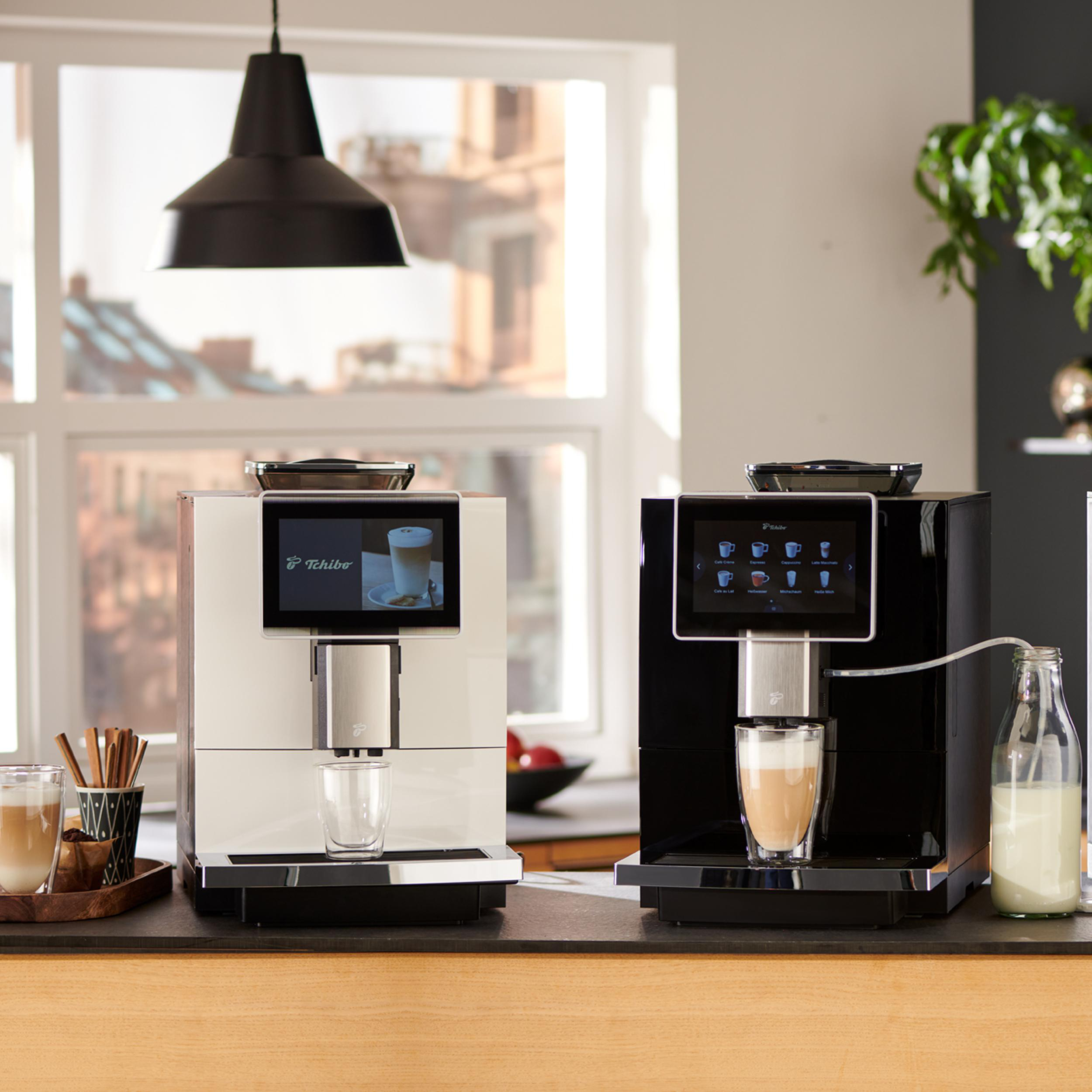 Zwei Kaffeemaschinen in einer Küche. Eine ist weiß, die andere schwarz, beide mit Touchscreens.