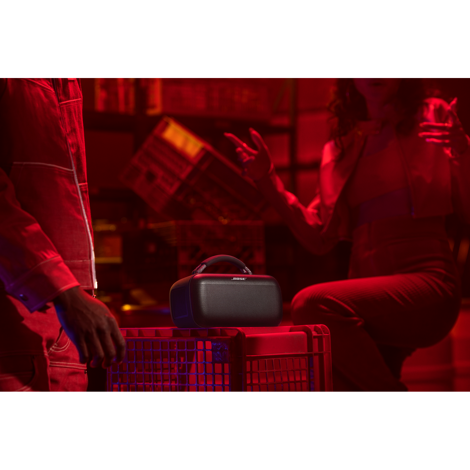 Man and woman in a red-lit room, a speaker on a red crate. Party scene.