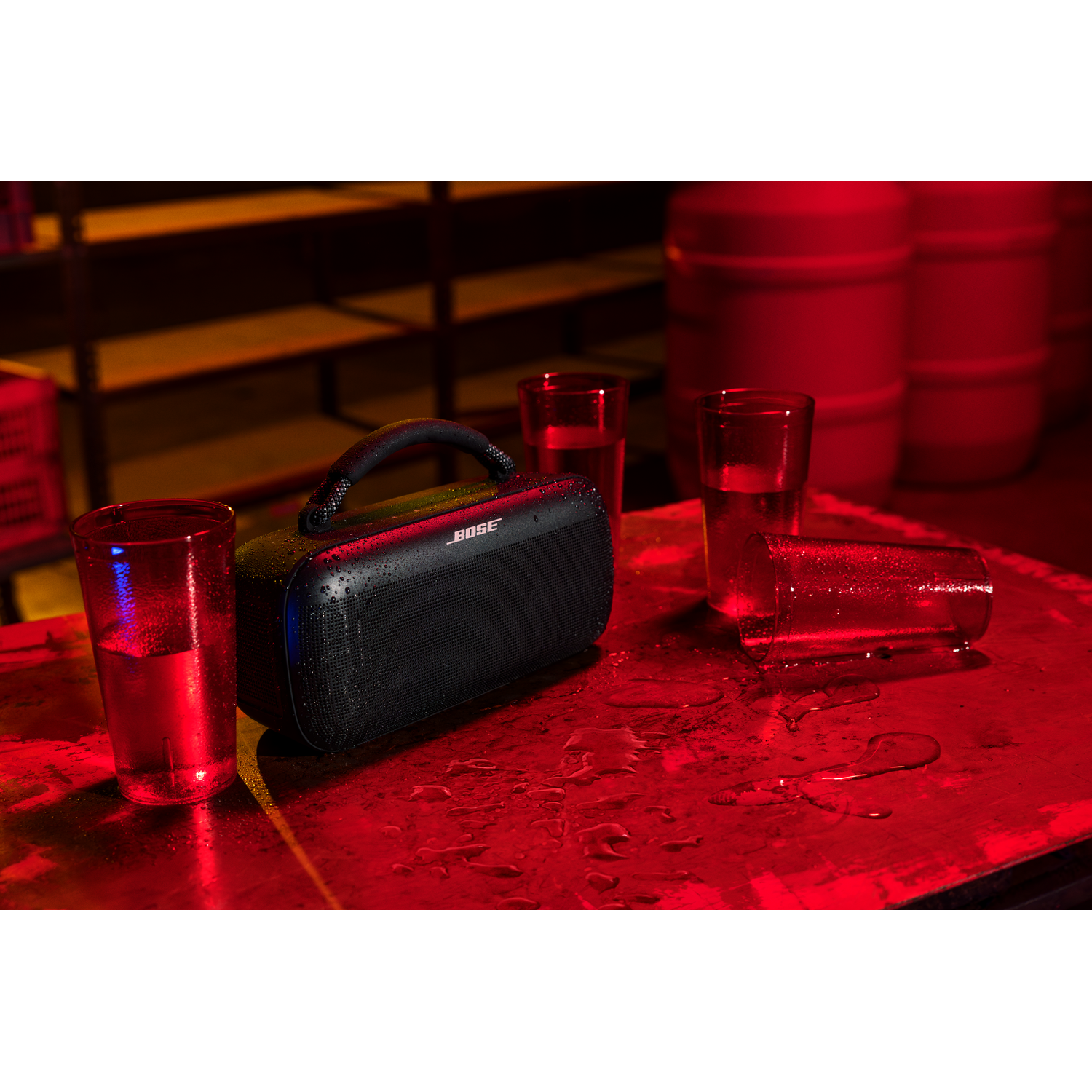 A black Bose speaker on a red table, with water and glasses around it.