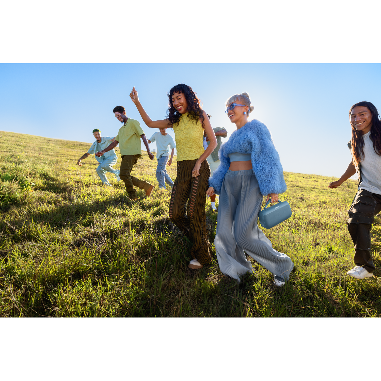 Een groep mensen die dansen op een groen veld, met een blauwe luidspreker op de voorgrond.