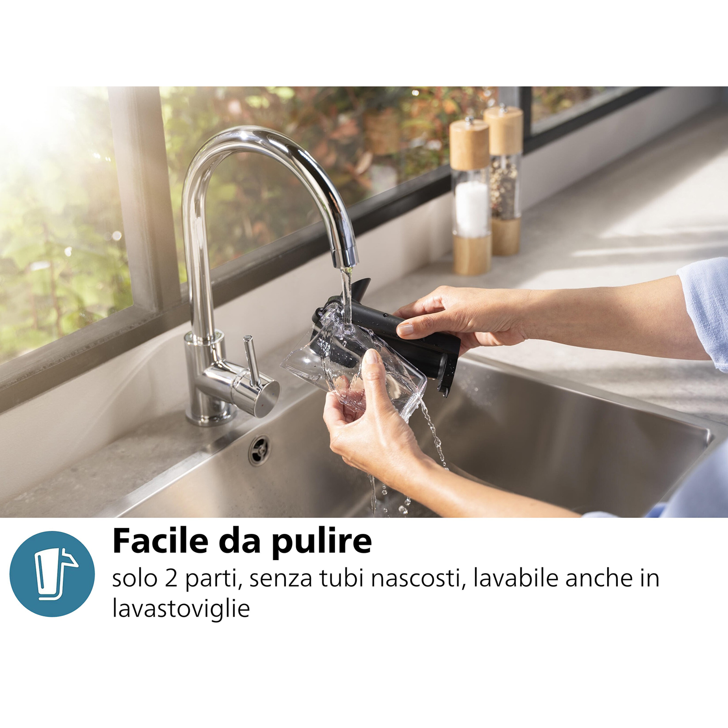 Una persona pulisce un dispositivo nero sotto l'acqua corrente in un lavandino in acciaio inossidabile.