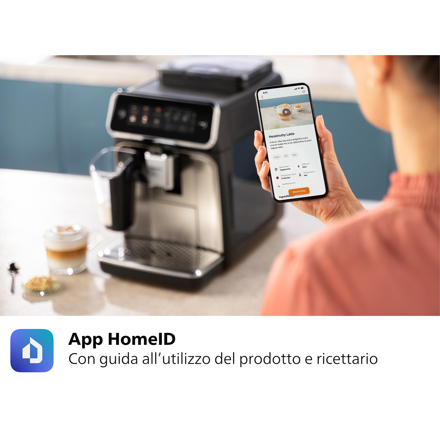 Persona che tiene uno smartphone accanto a una macchina da caffè nera con latte art.