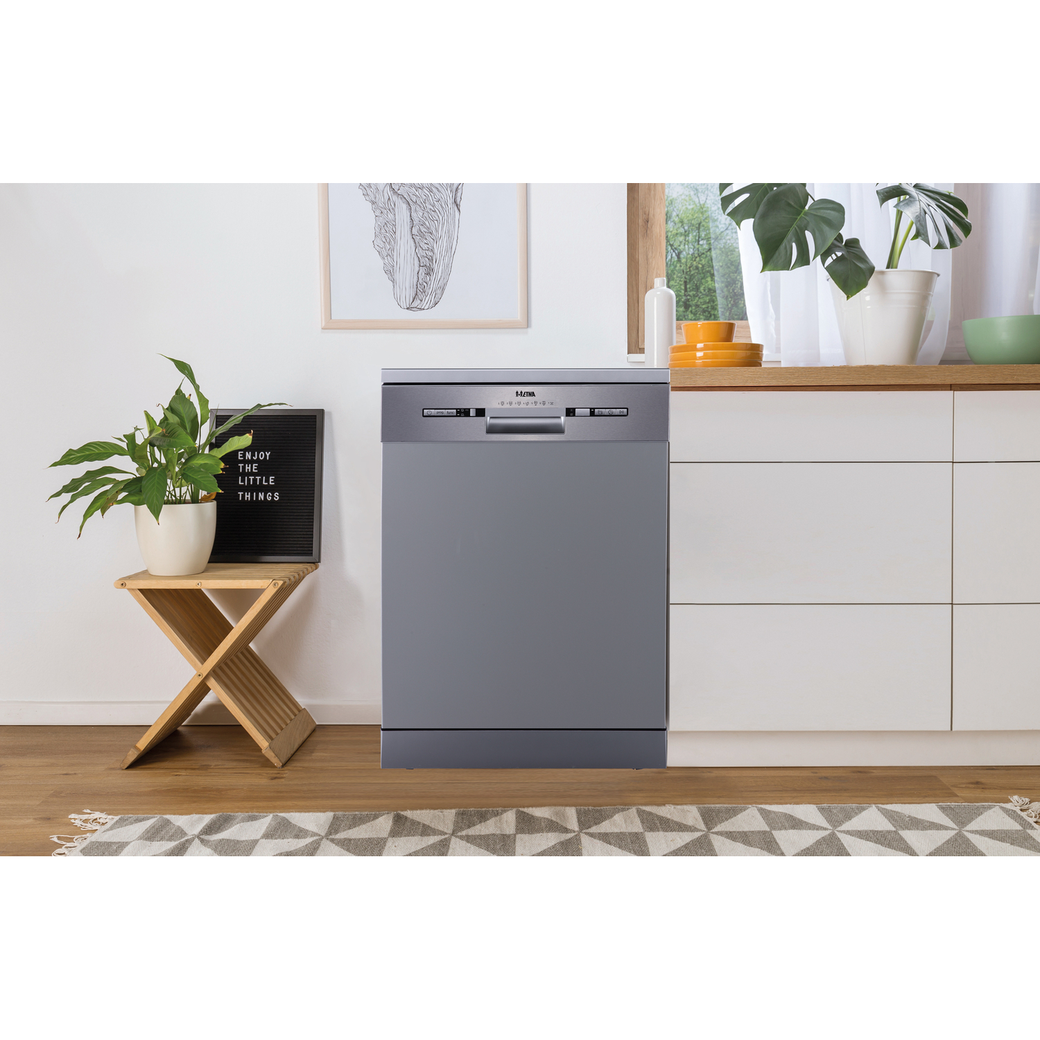 A gray dishwasher in a kitchen setting. A plant and artwork are to the left. White cabinets on right.