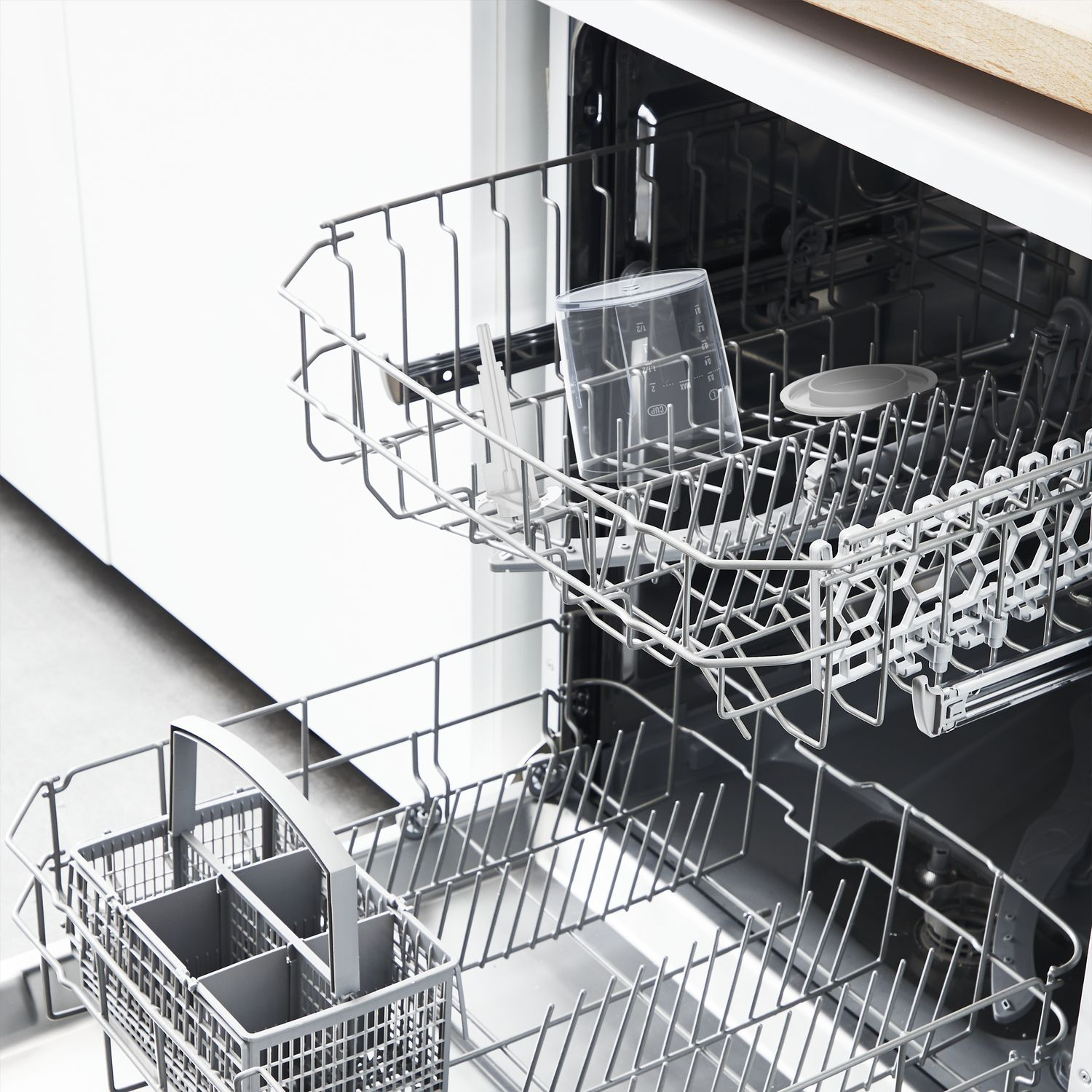 Dishwasher interior with two racks. A clear measuring cup and a utensil basket are visible.