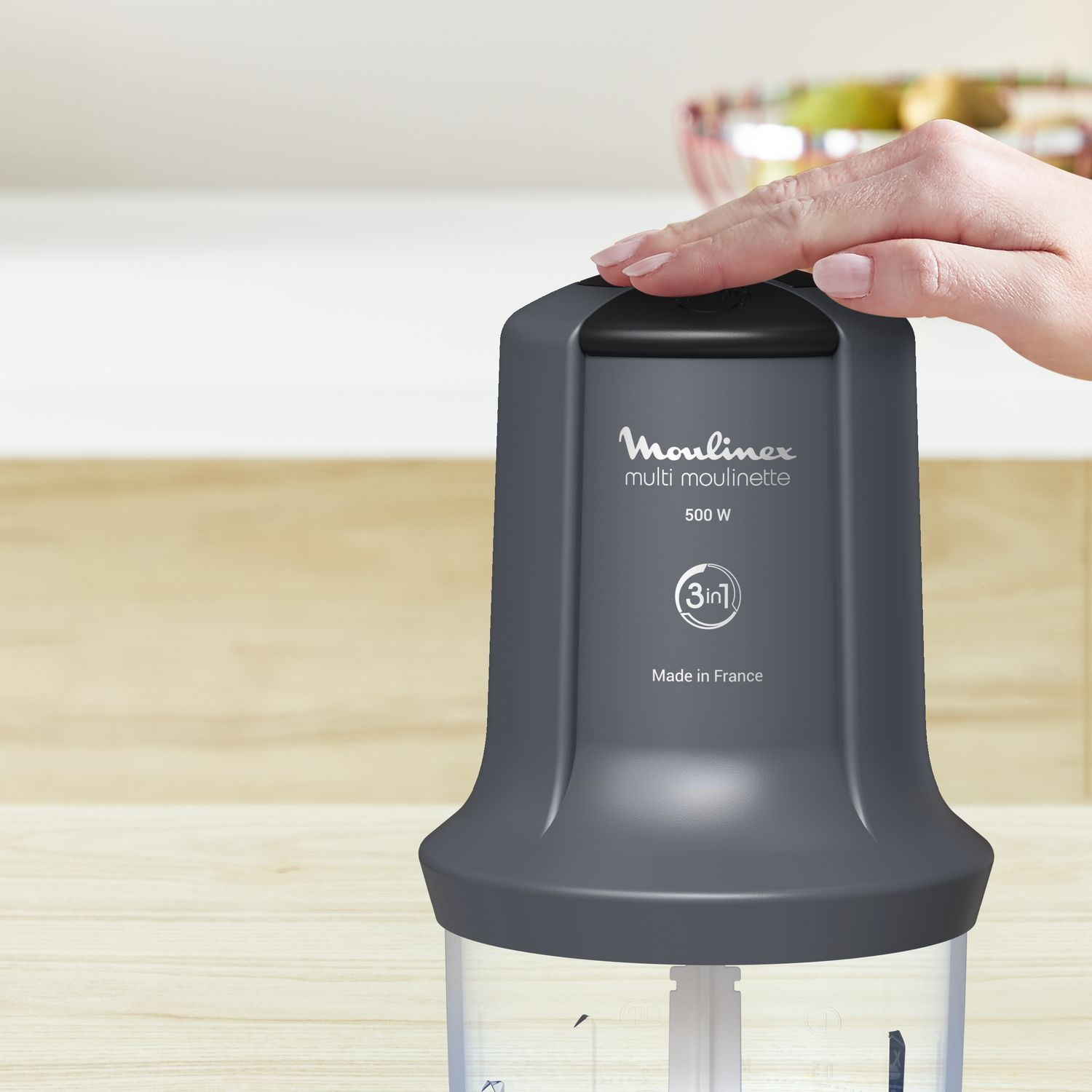 Hand touches a dark gray Moulinex multi moulinette on a wooden surface.