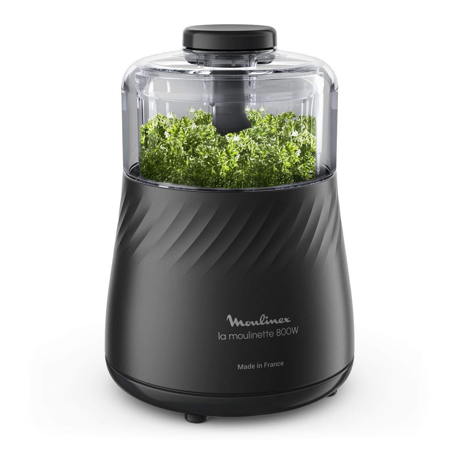 A black food processor with parsley inside is shown against a white background.