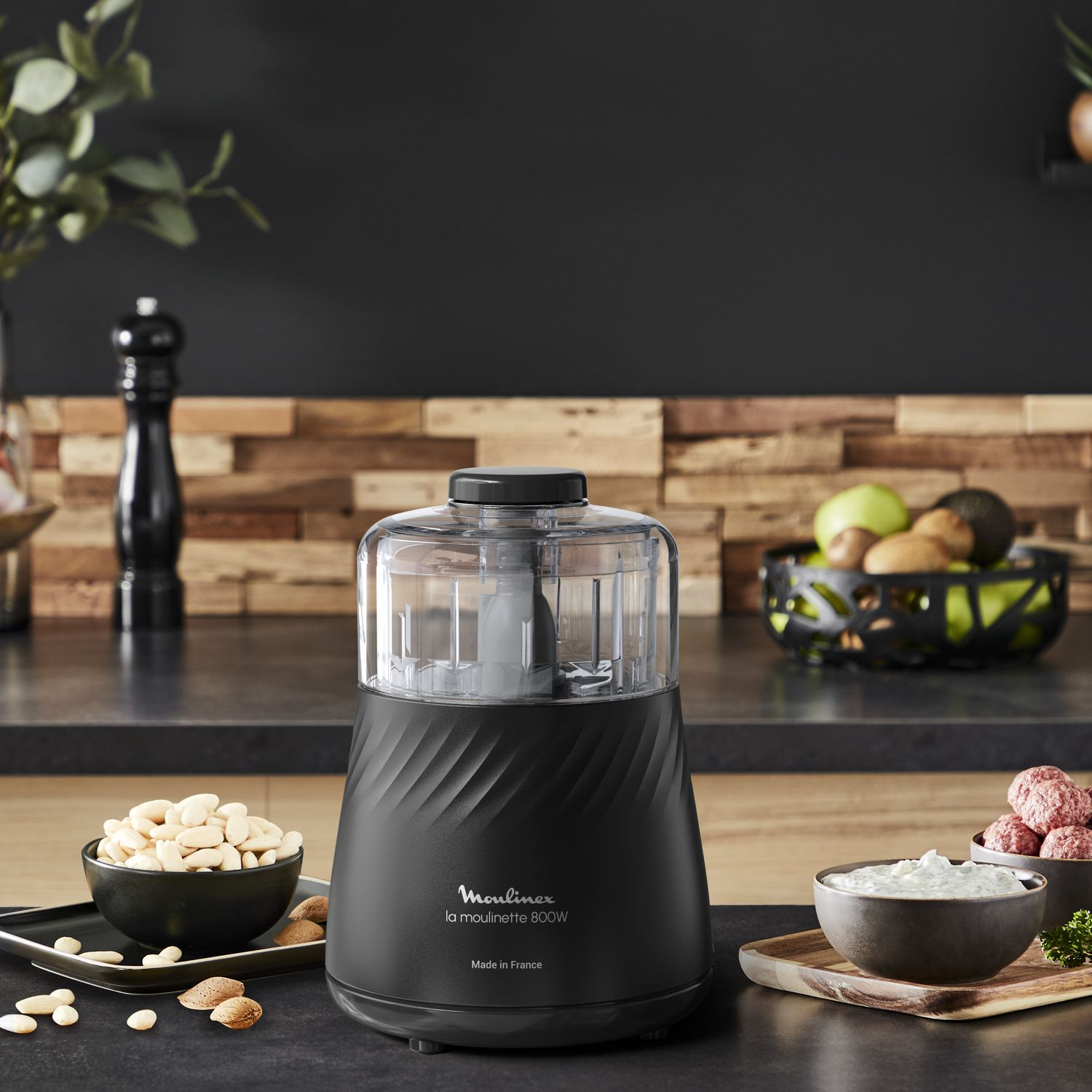 Black food processor with ingredients and a black wooden background.