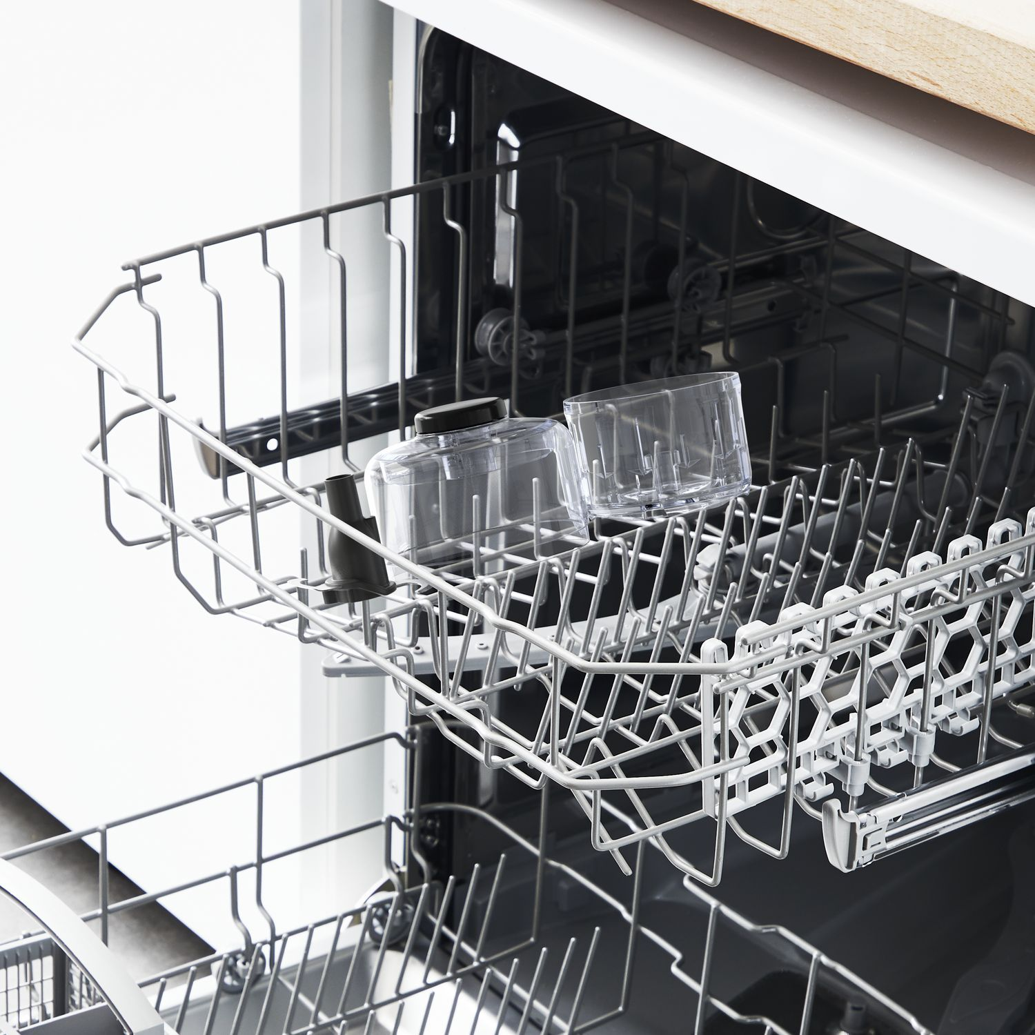 Dishwasher rack with two clear glasses inside. The rack is in an open, white dishwasher.