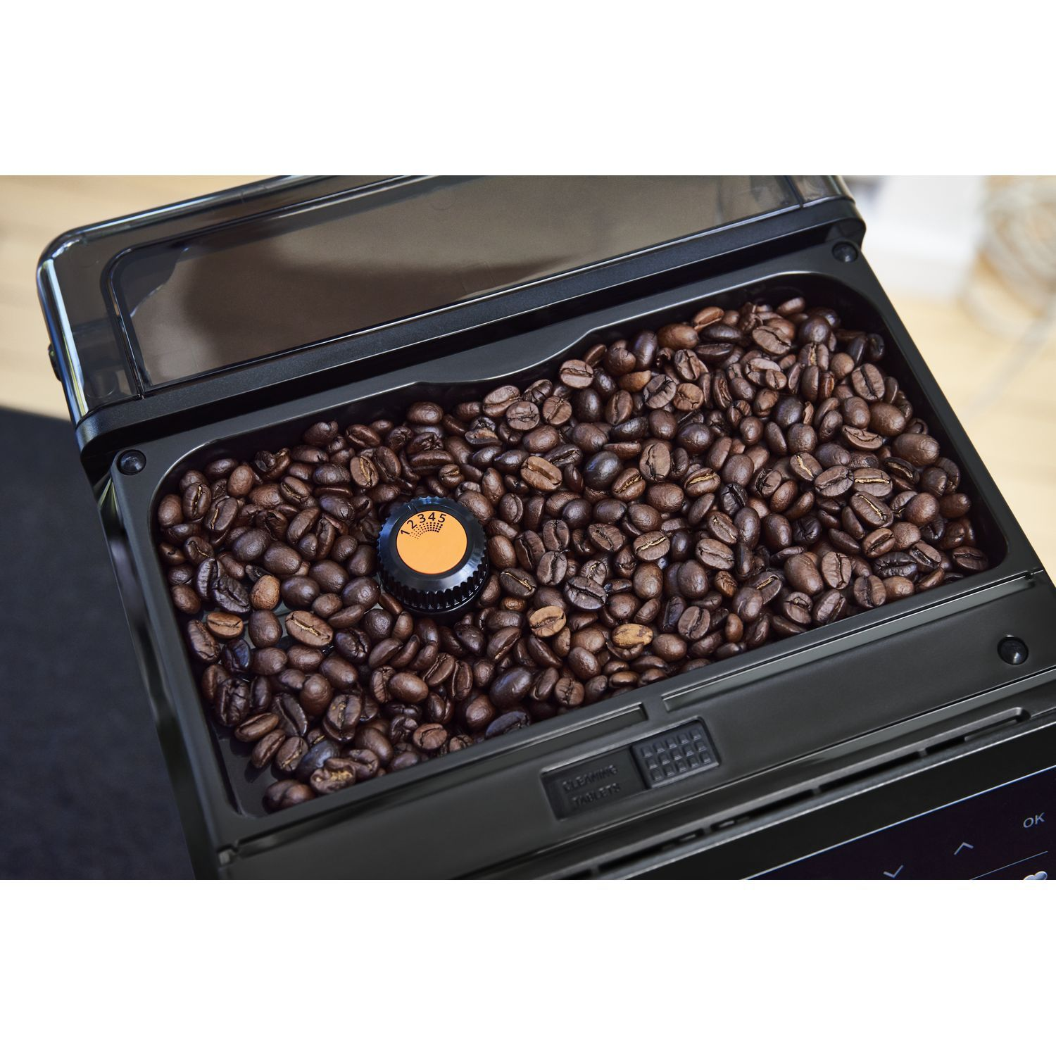 Coffee beans fill the open container of a coffee machine. A dial is in the middle.