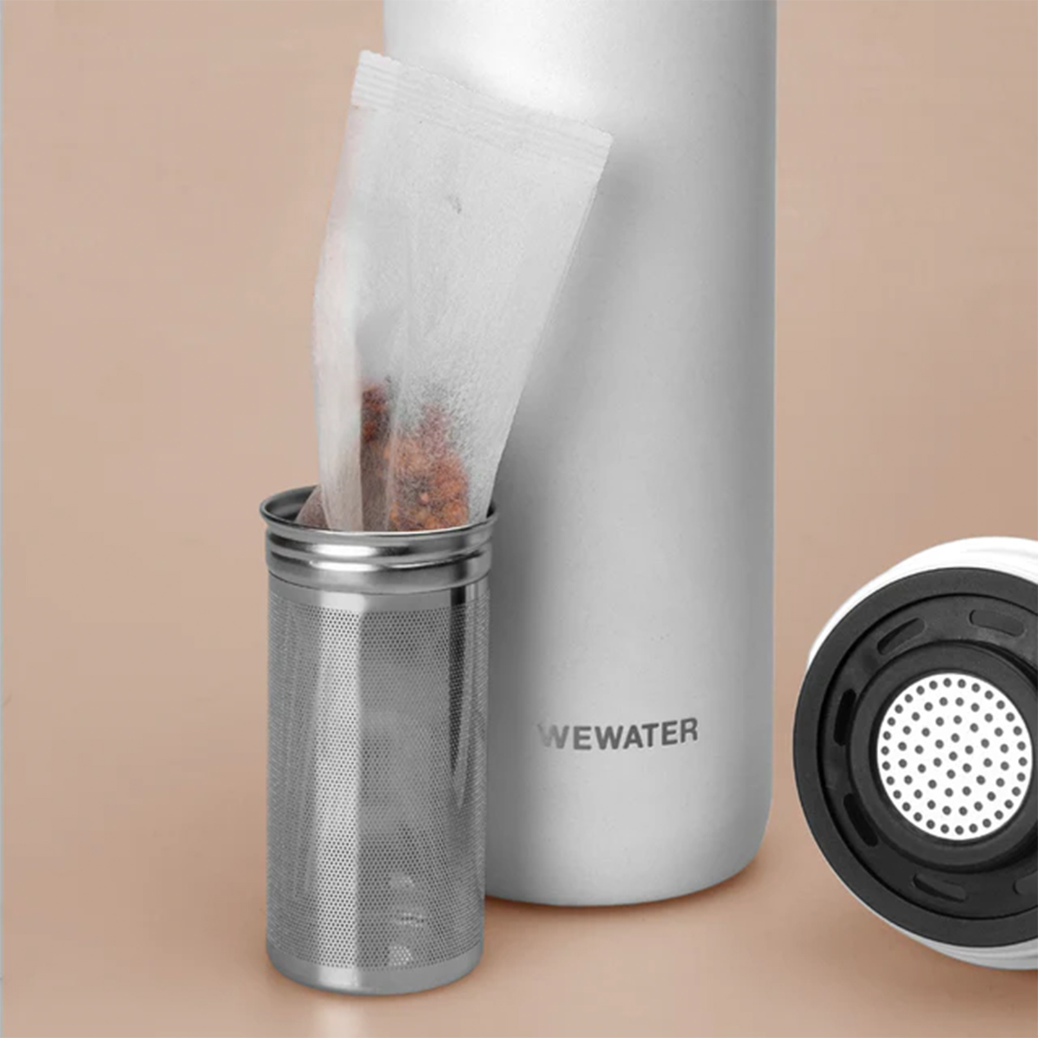 Un infusore per tè WeWater con una bustina di tè all'interno, accanto a una bottiglia d'acqua bianca.