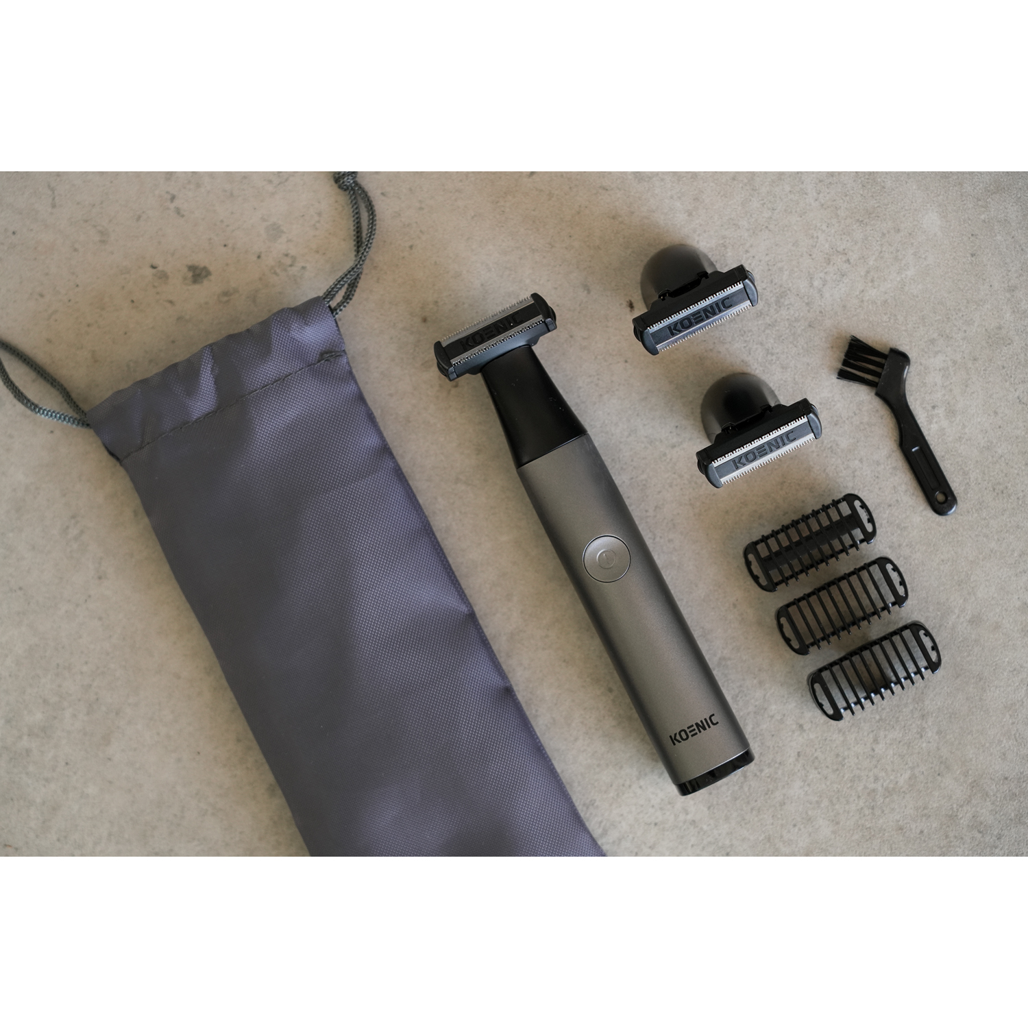 Kit per la cura del corpo con trimmer, accessori e una borsa grigia. Gli articoli sono su una superficie grigia.