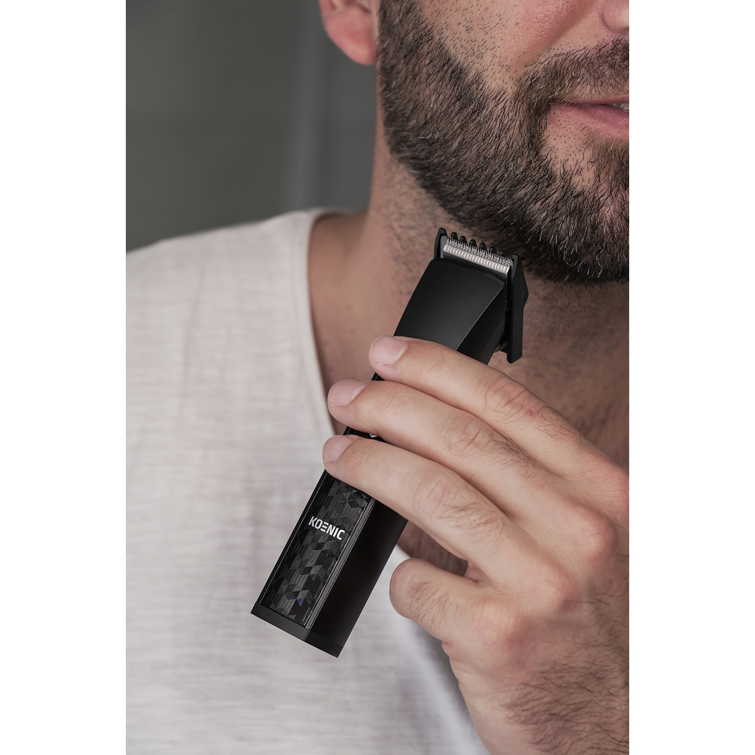 Un uomo si taglia la barba con un tagliabarba nero. Il trimmer è nella sua mano.