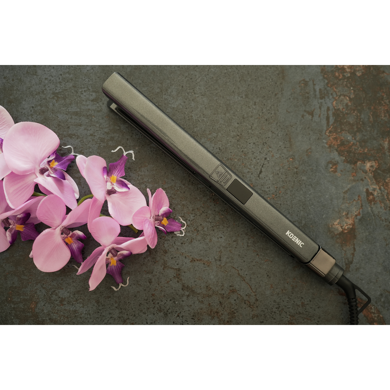 Una piastra per capelli con orchidee rosa su una superficie grigia strutturata.