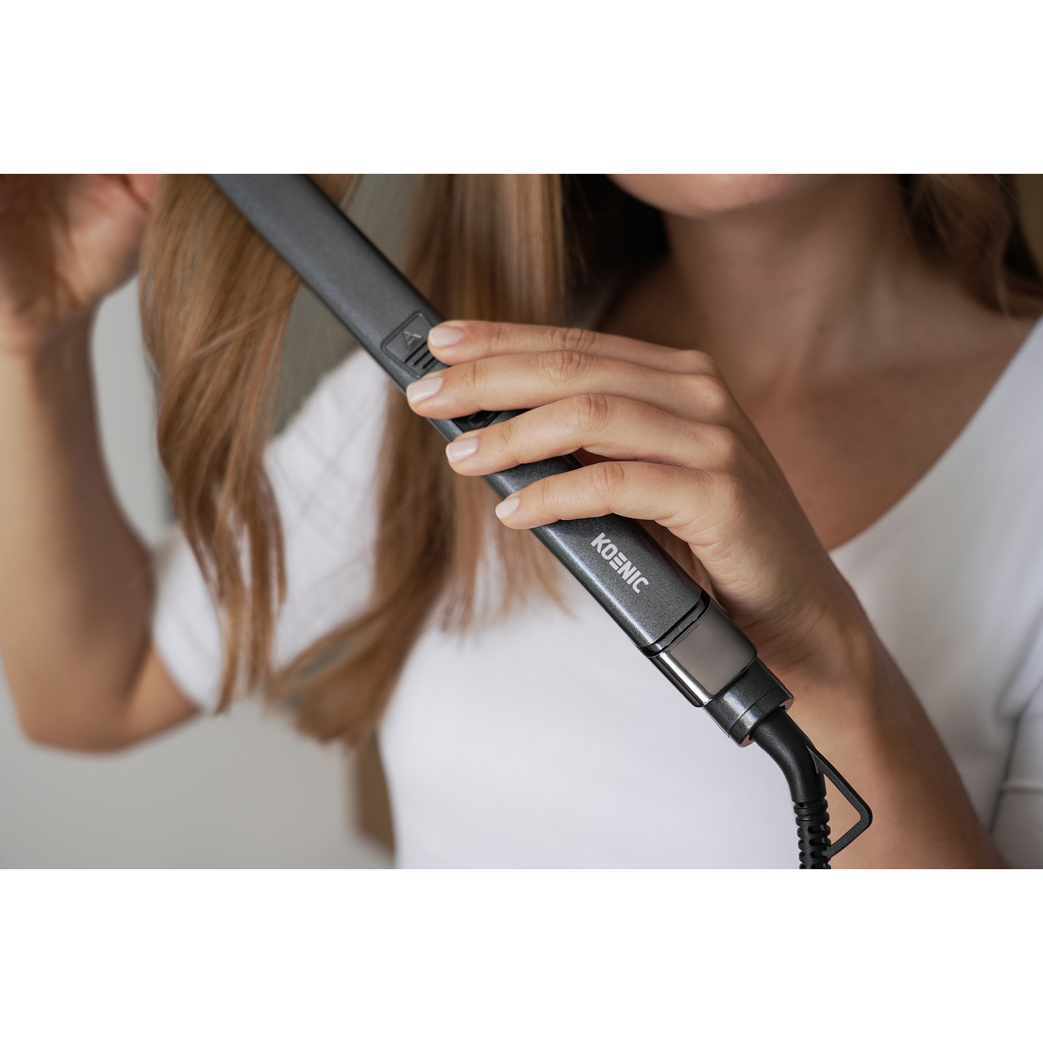 Una persona che usa una piastra per capelli grigia sui propri capelli, primo piano.