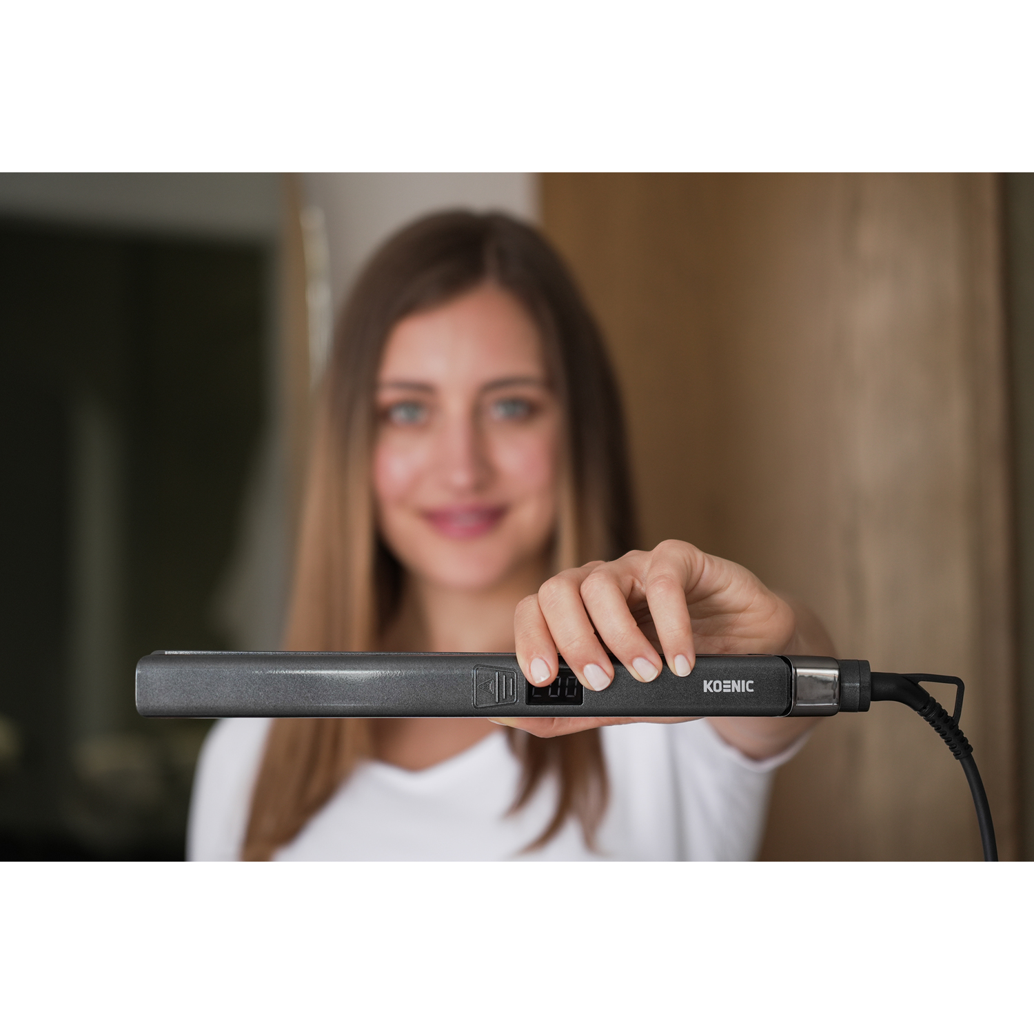 Donna che tiene una piastra per capelli grigio scuro, sorridendo alla fotocamera.