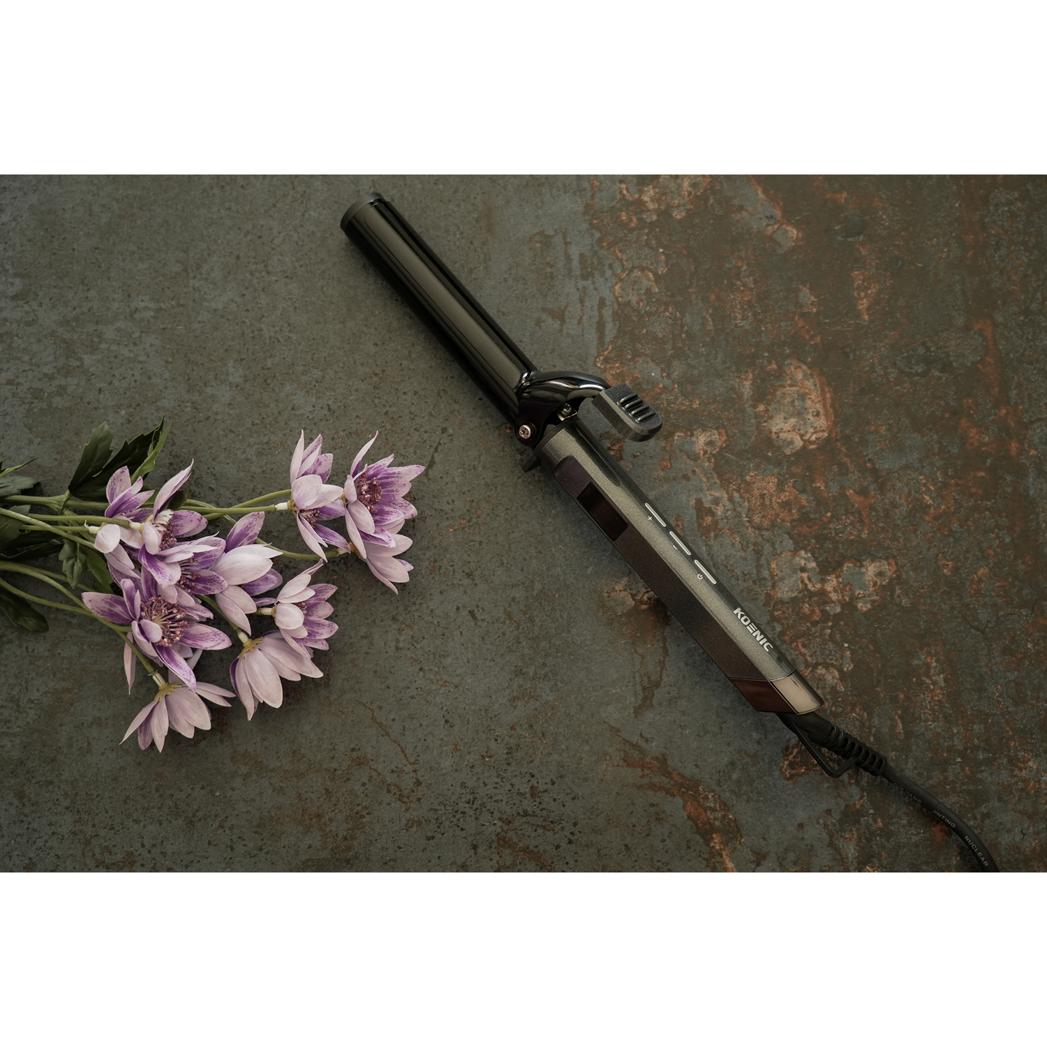 Arricciacapelli nero con manico nero e bouquet di fiori viola, su superficie grigia.