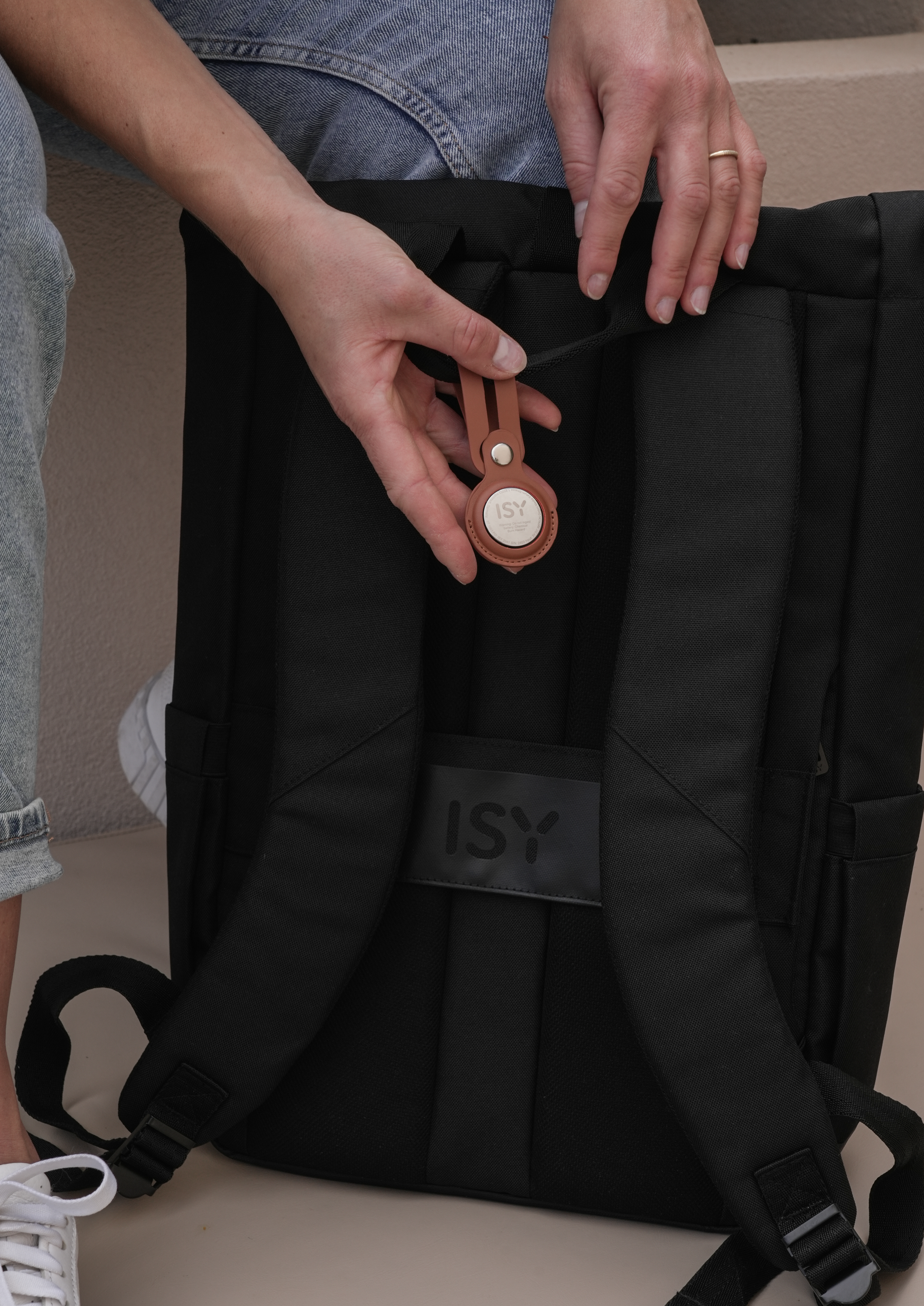 Eine Person hält einen schwarzen Rucksack mit einem braunen AirTag.