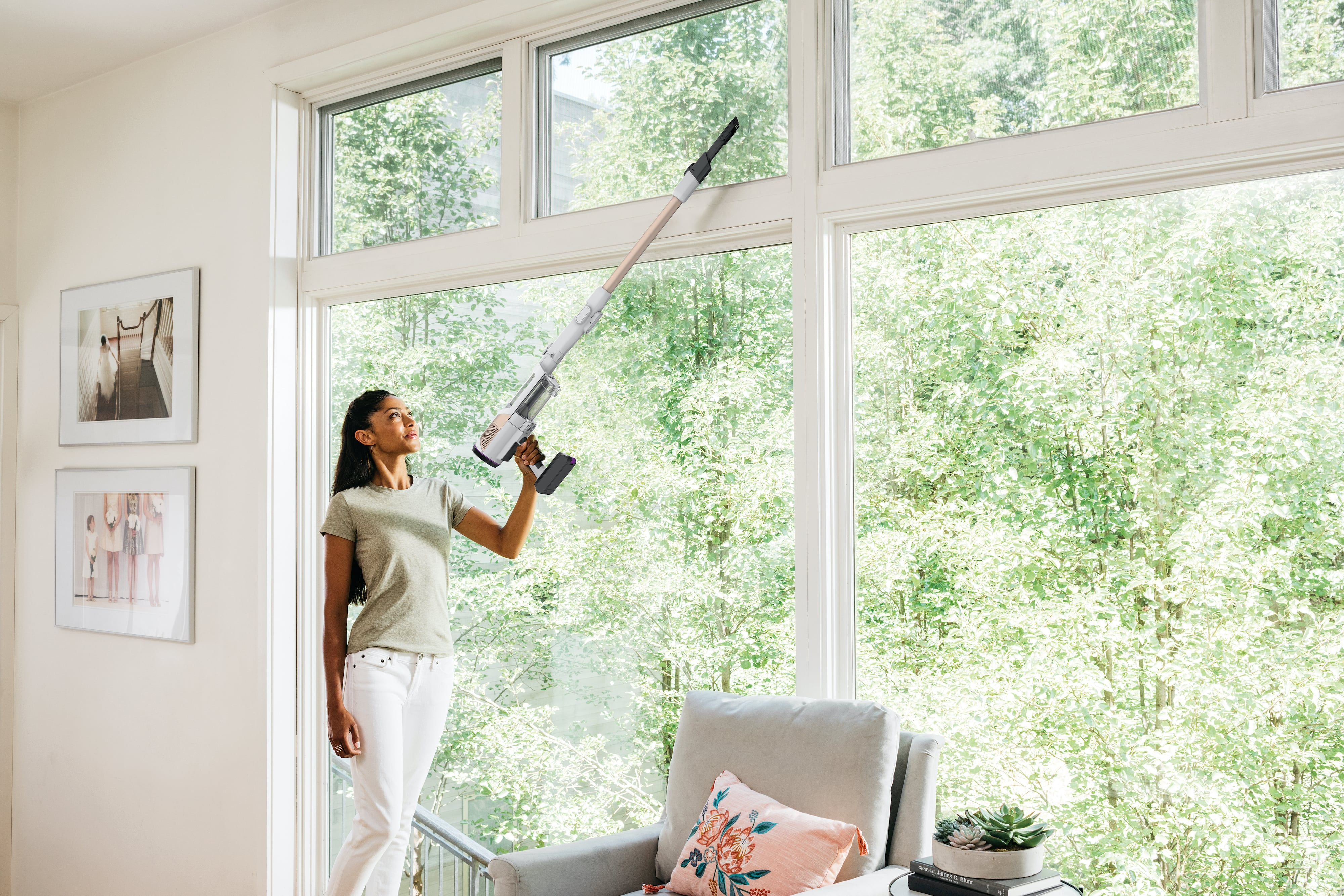 Frau, die mit einem Stielsauger ein Fenster saugt. Fenster und Bäume sind im Hintergrund sichtbar.