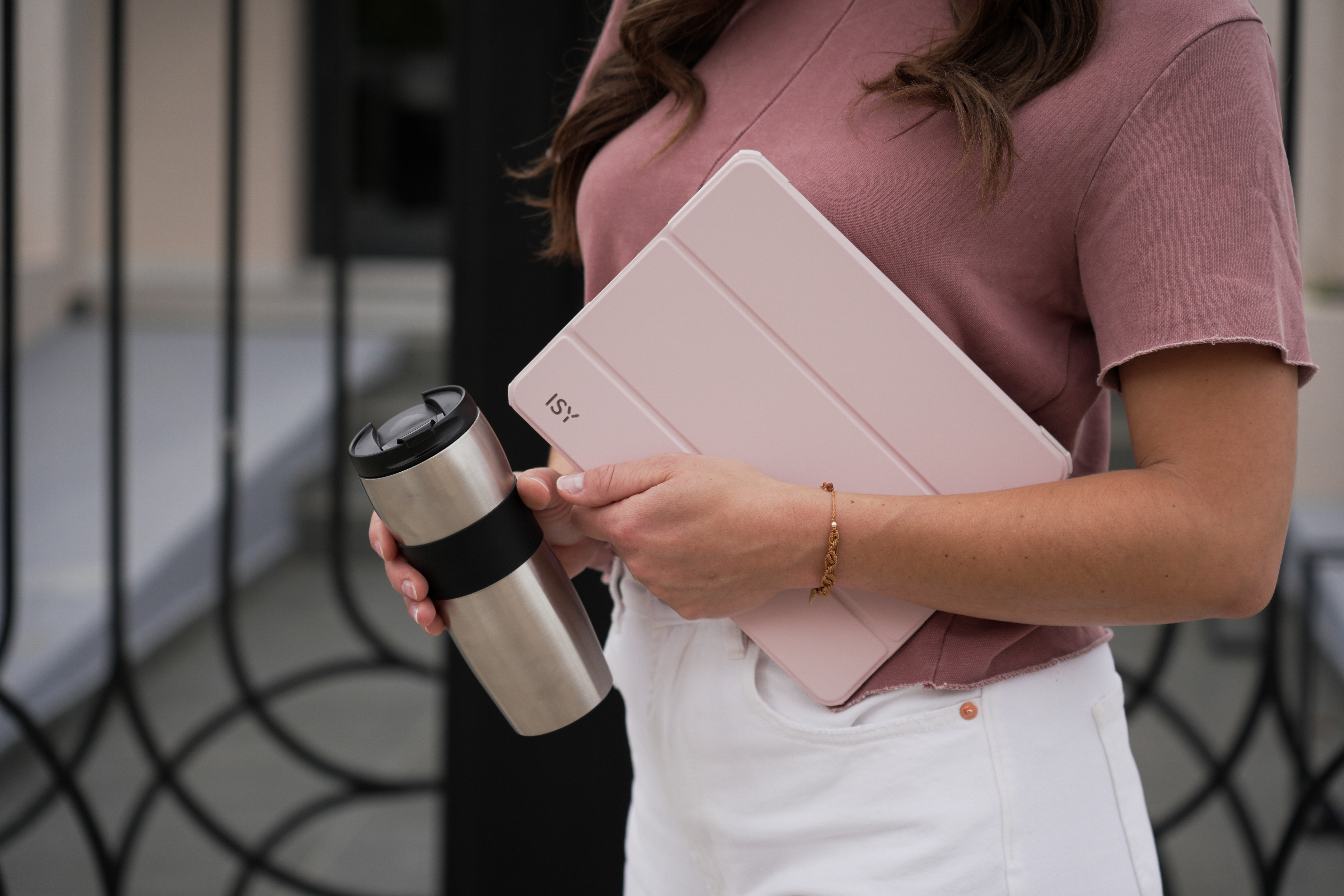 Frau hält ein Tablet und einen silbernen Reisebecher; unscharfer Hintergrund.