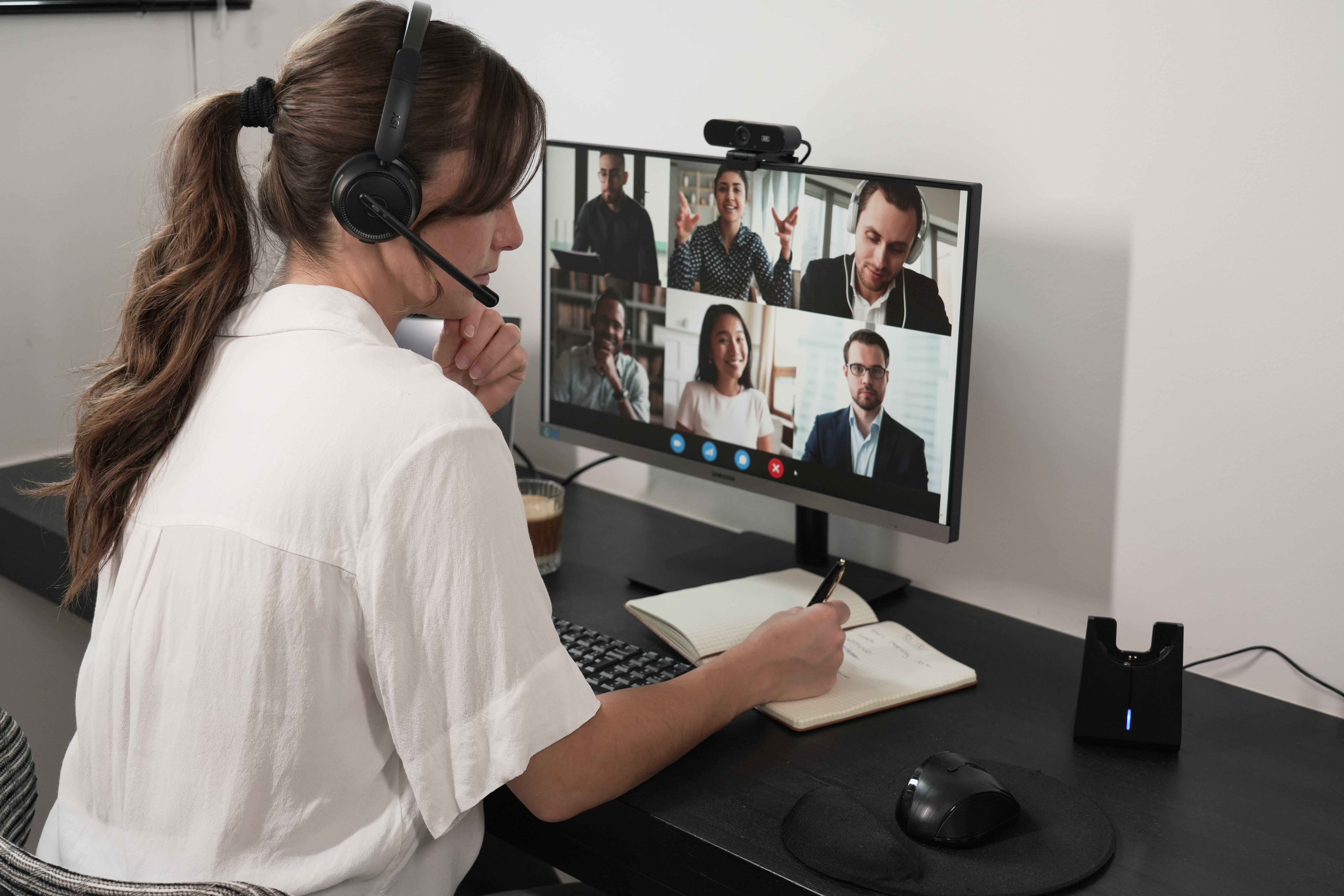 Eine Frau benutzt einen Computer für einen Videoanruf. Sie trägt ein Headset und schaut auf den Bildschirm.